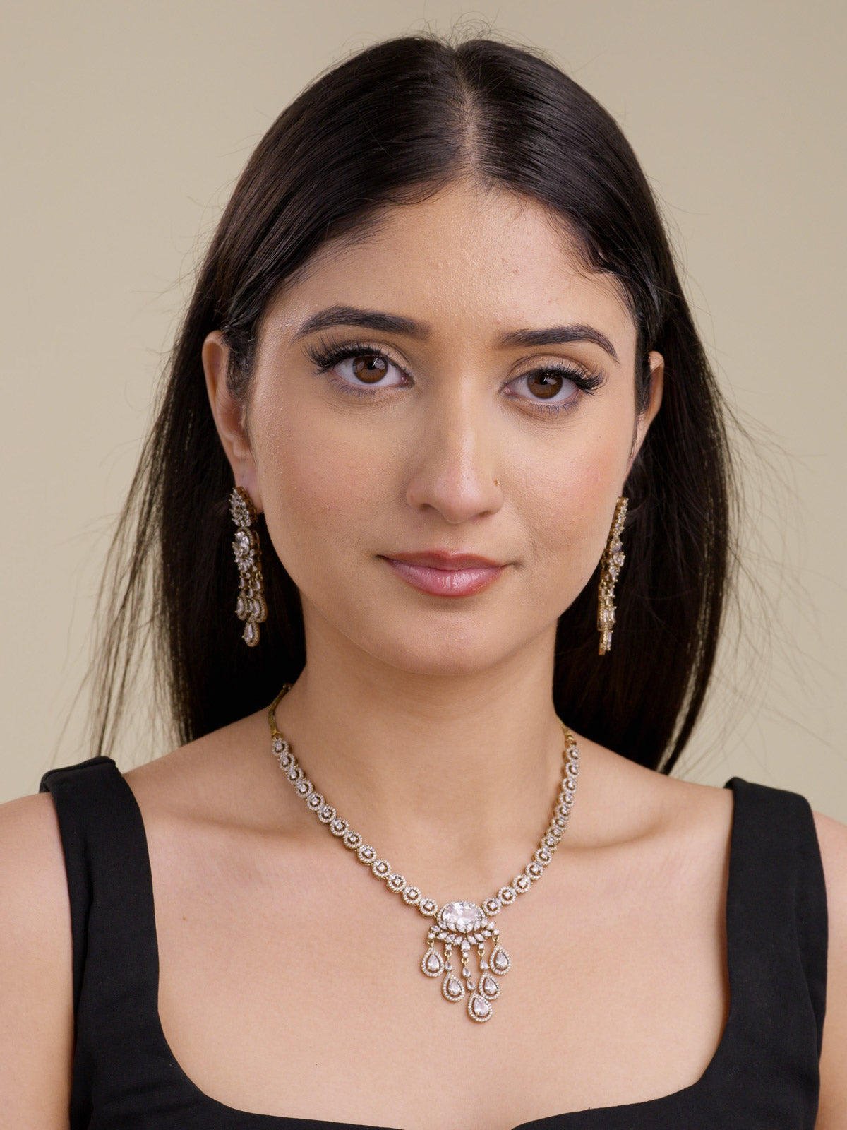 Model wearing an antique gold tone American Diamond necklace set with round CZ stone links, a clear oval centre stone, clear teardrop accents, matching drop earrings, and a black outfit in a front portrait shot.