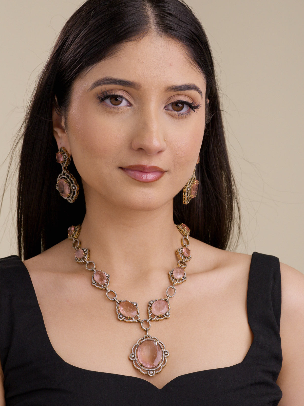 Model wearing a Fusion necklace set with peach-neutral stones, American Diamond-style detailing, antique gold tone setting, and matching drop earrings in a front portrait image.