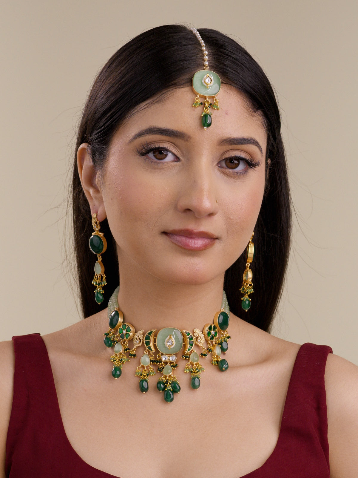 Front view of model wearing the Sage Green Fusion necklace set with matching earrings and maang tikka, sage bead strands, matte gold tone detailing, pale sage centre accent, dark green drops, peacock motif details, green floral sections, and hanging bead clusters.