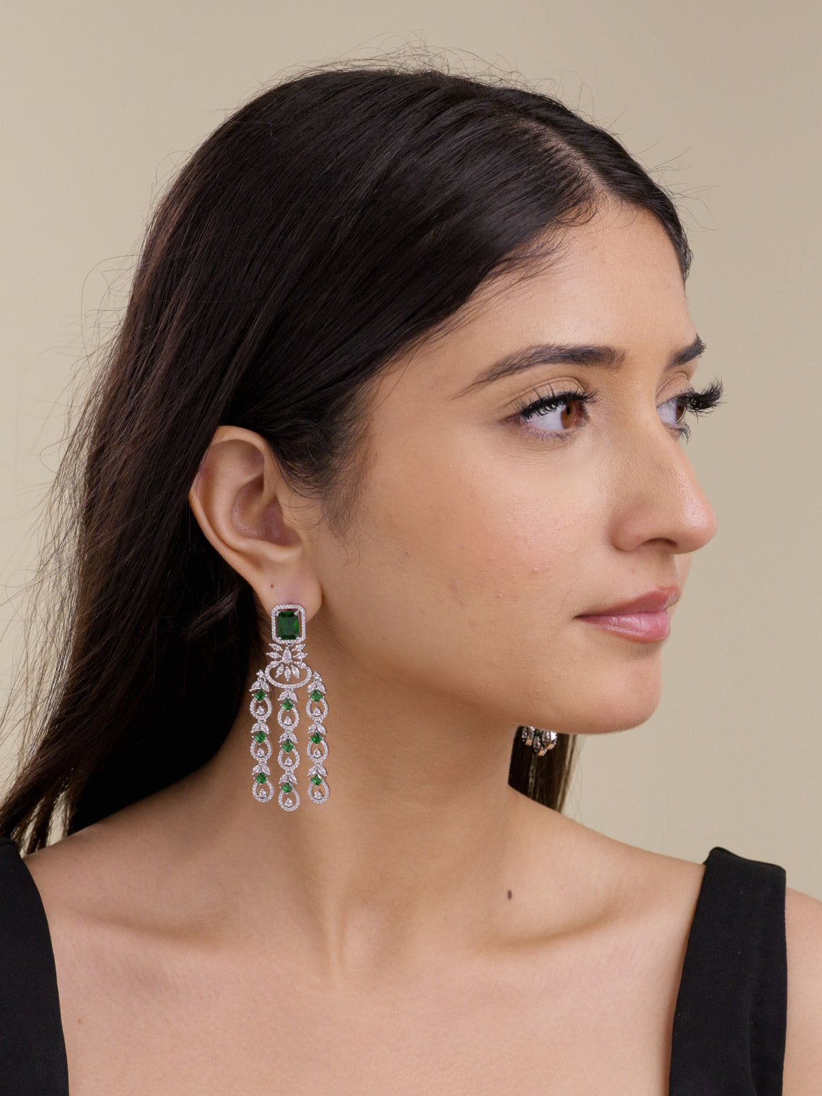 Model wearing a silver tone American Diamond earring with a green square stud, clear CZ stones, curved centre accent, and three hanging teardrop strands in a side portrait shot.