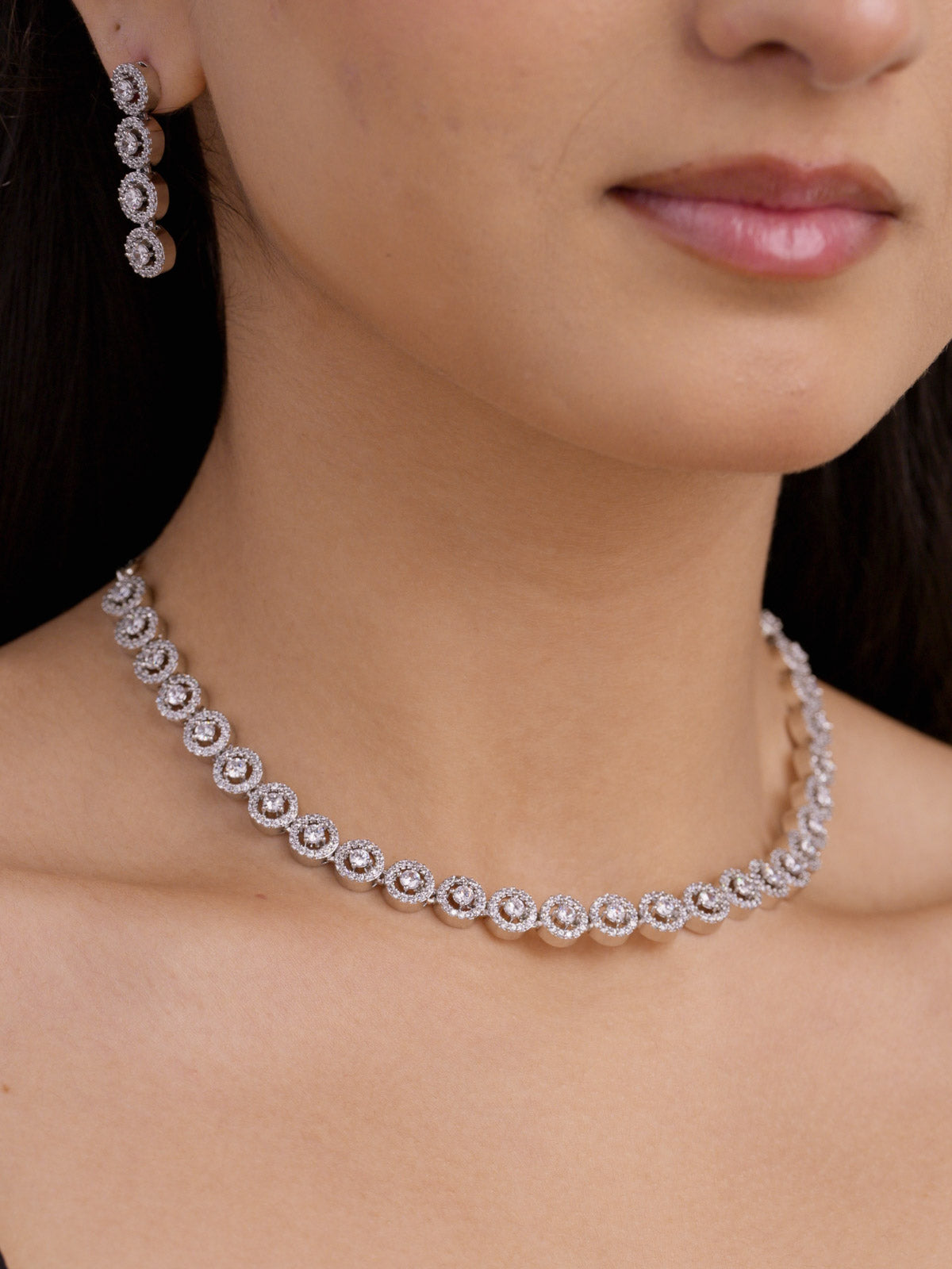 Close-up of american diamond necklace with fine round halo-style stones in silver tone with matching drop earrings on model