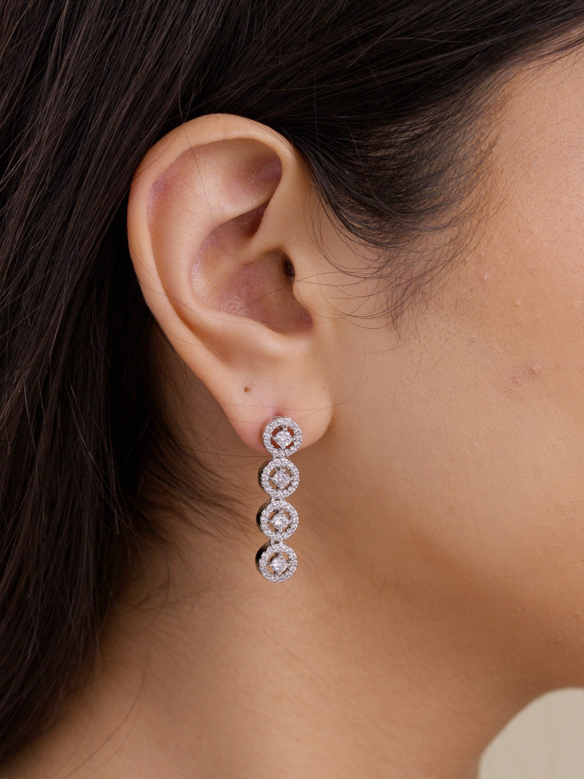 Close-up of american diamond drop earrings with fine round halo-style stones in silver tone on model ear