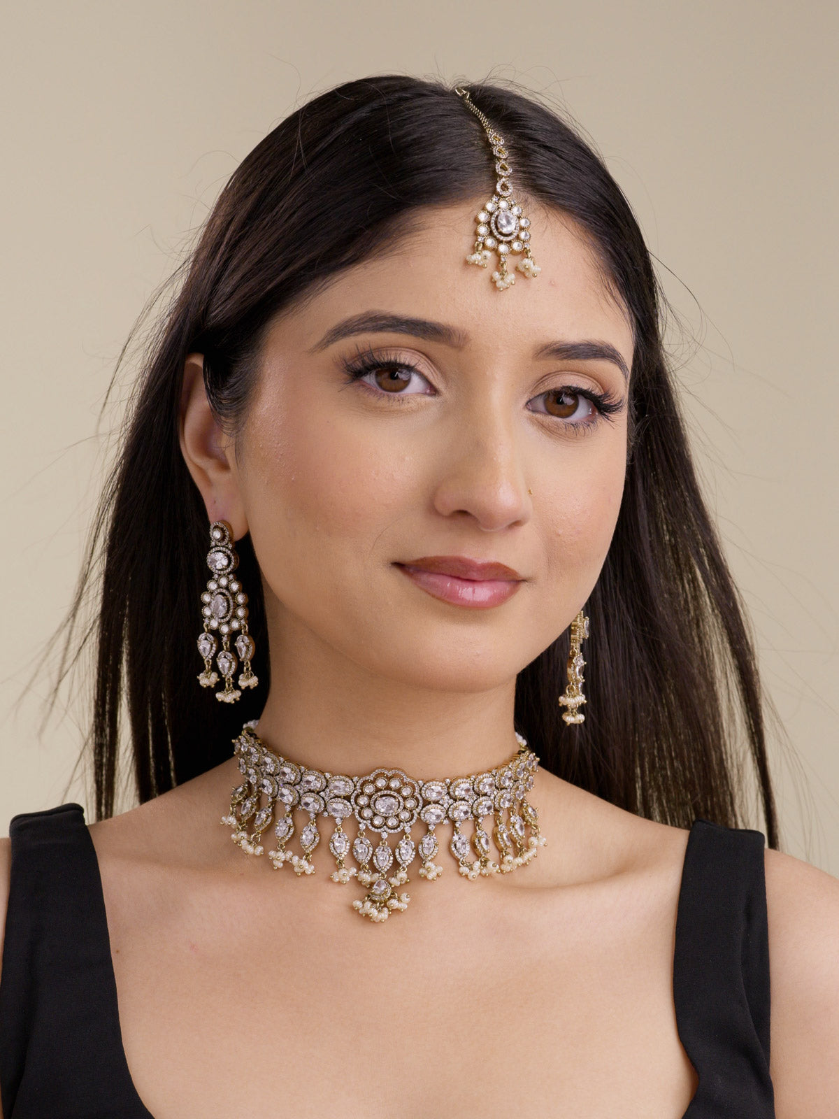 Model wearing an antique gold tone American Diamond choker necklace set with neutral stones, matching earrings, maang tikka, and pearl-style drops.