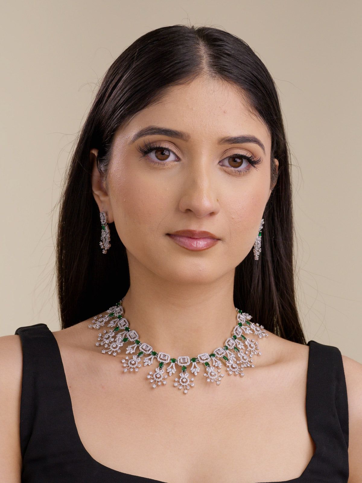 Model wearing a silver tone American Diamond necklace set with green oval stones, matching earrings, square stone links, and floral-inspired drop detailing.