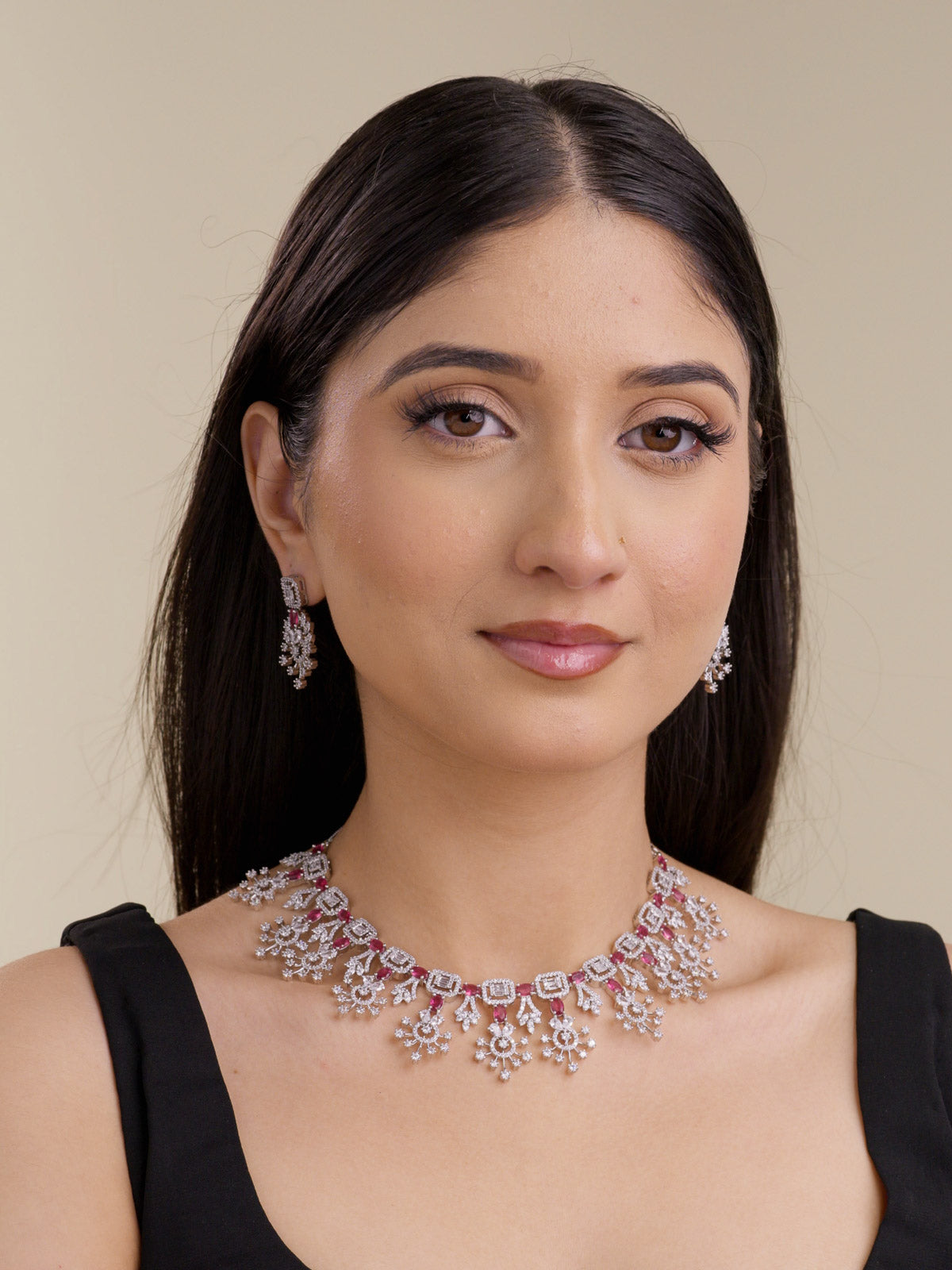 Model wearing a silver tone American Diamond necklace set with ruby red stones, matching earrings, square stone links, and floral-inspired drop detailing.
