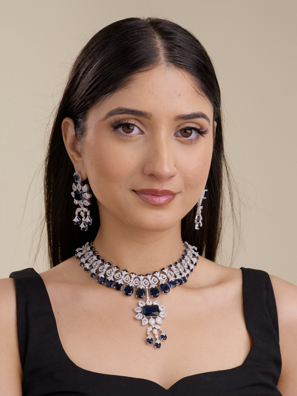 Model wearing a blue American Diamond necklace set in silver tone with matching earrings, close choker placement, blue stone drops, and a centre pendant.