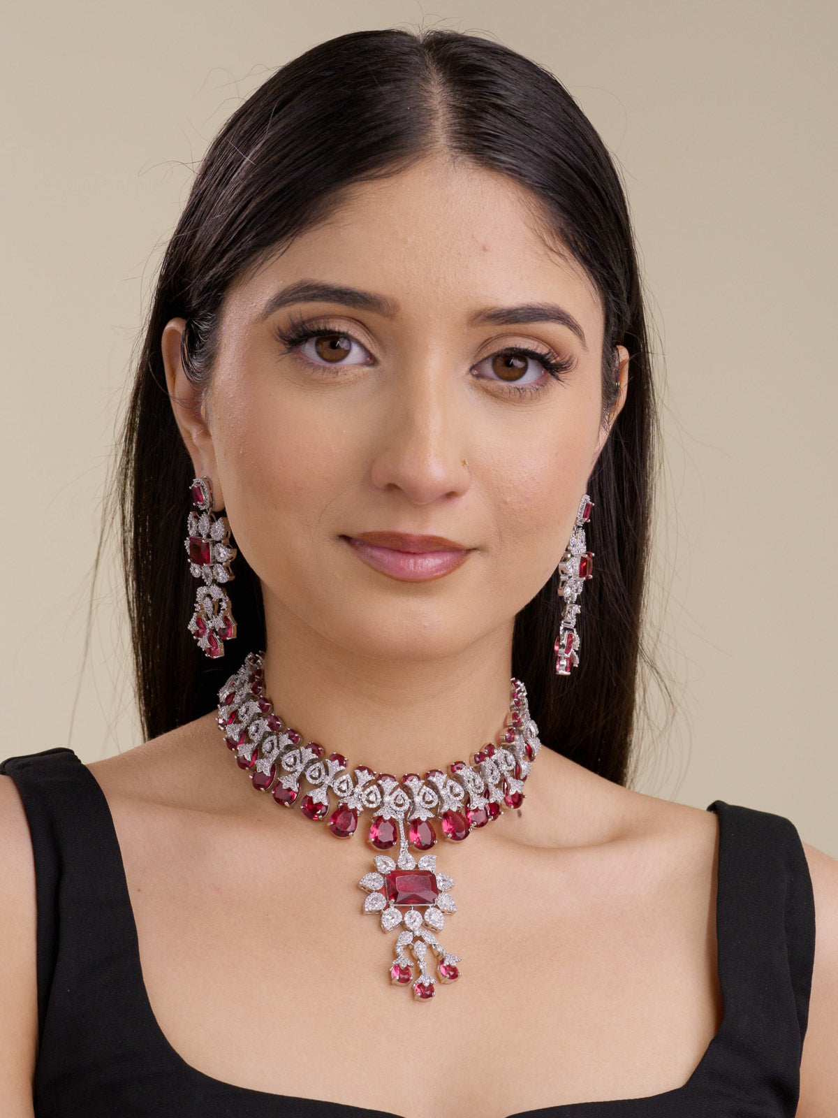 Model wearing a ruby-red American Diamond necklace set in silver tone with matching earrings, close choker placement, red stone drops, and a centre pendant.