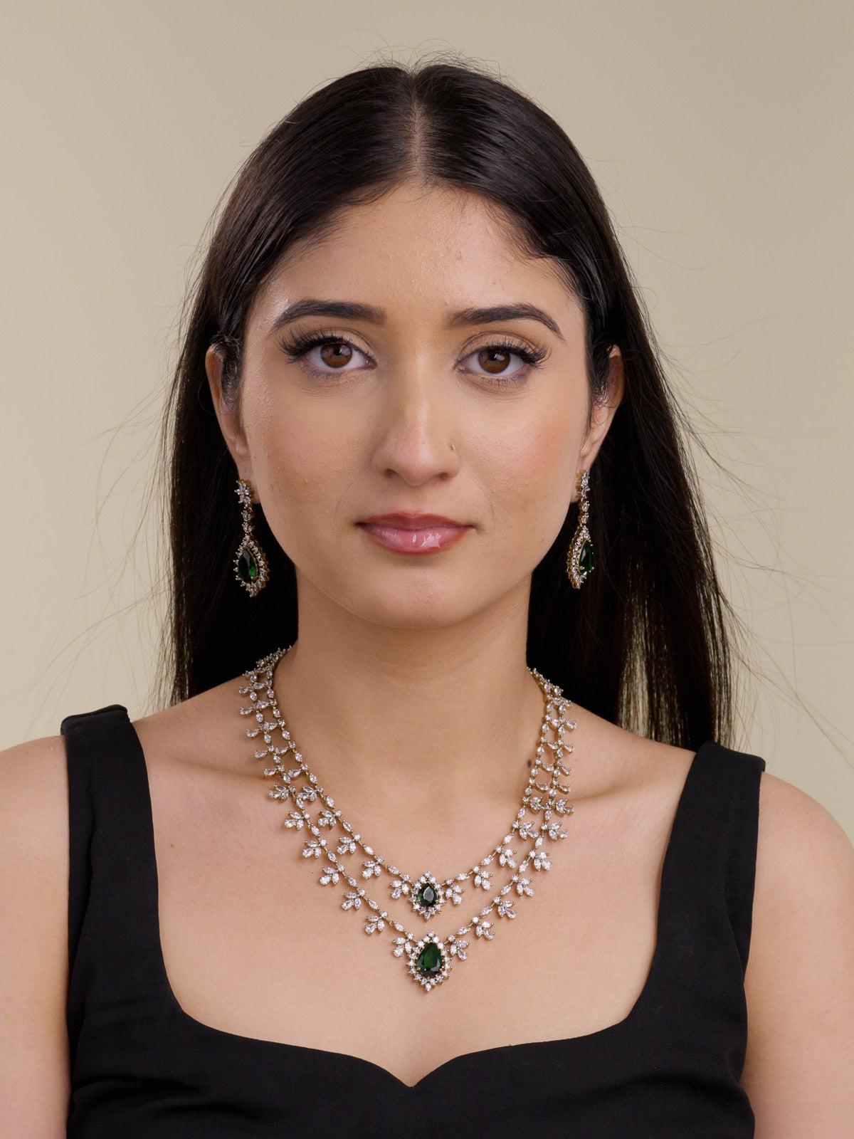 Model wearing an antique gold tone American Diamond necklace set with two-strand layered CZ stone trails, floral-style clusters, green teardrop centre stones, and matching drop earrings in a front portrait shot.