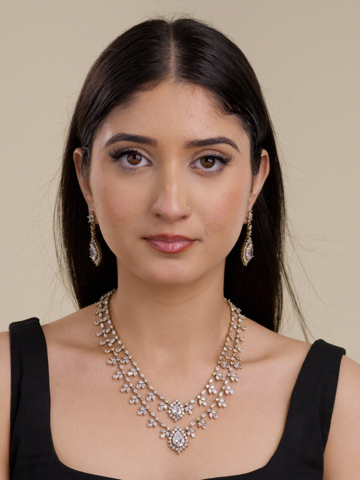 Model wearing an antique gold tone American Diamond necklace set with two-strand layered CZ stone trails, floral-style clusters, clear teardrop centre stones, and matching drop earrings in a front portrait shot.