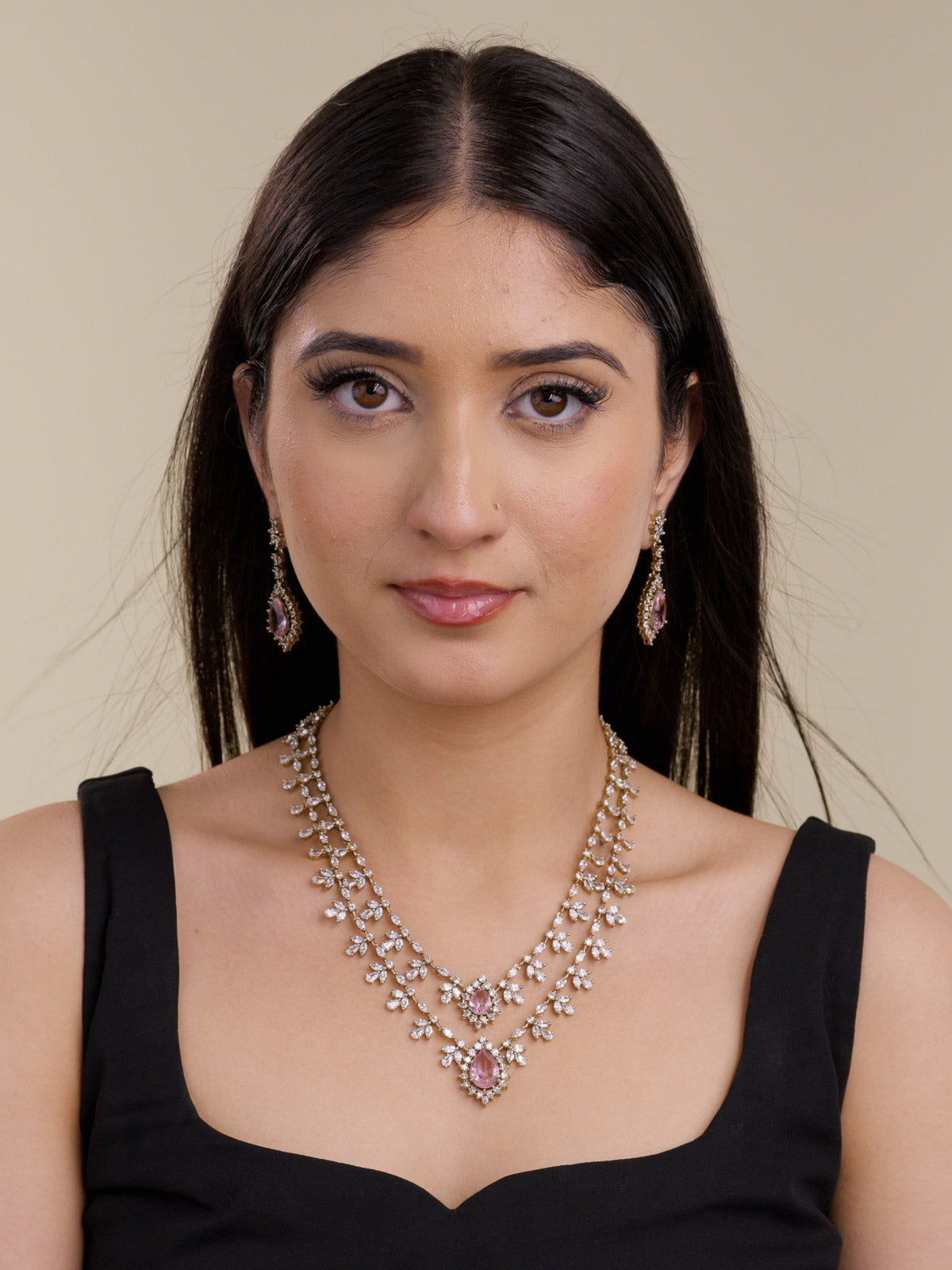 Model wearing an antique gold tone American Diamond necklace set with two-strand layered CZ stone trails, floral-style clusters, pink teardrop centre stones, and matching drop earrings in a front portrait shot.