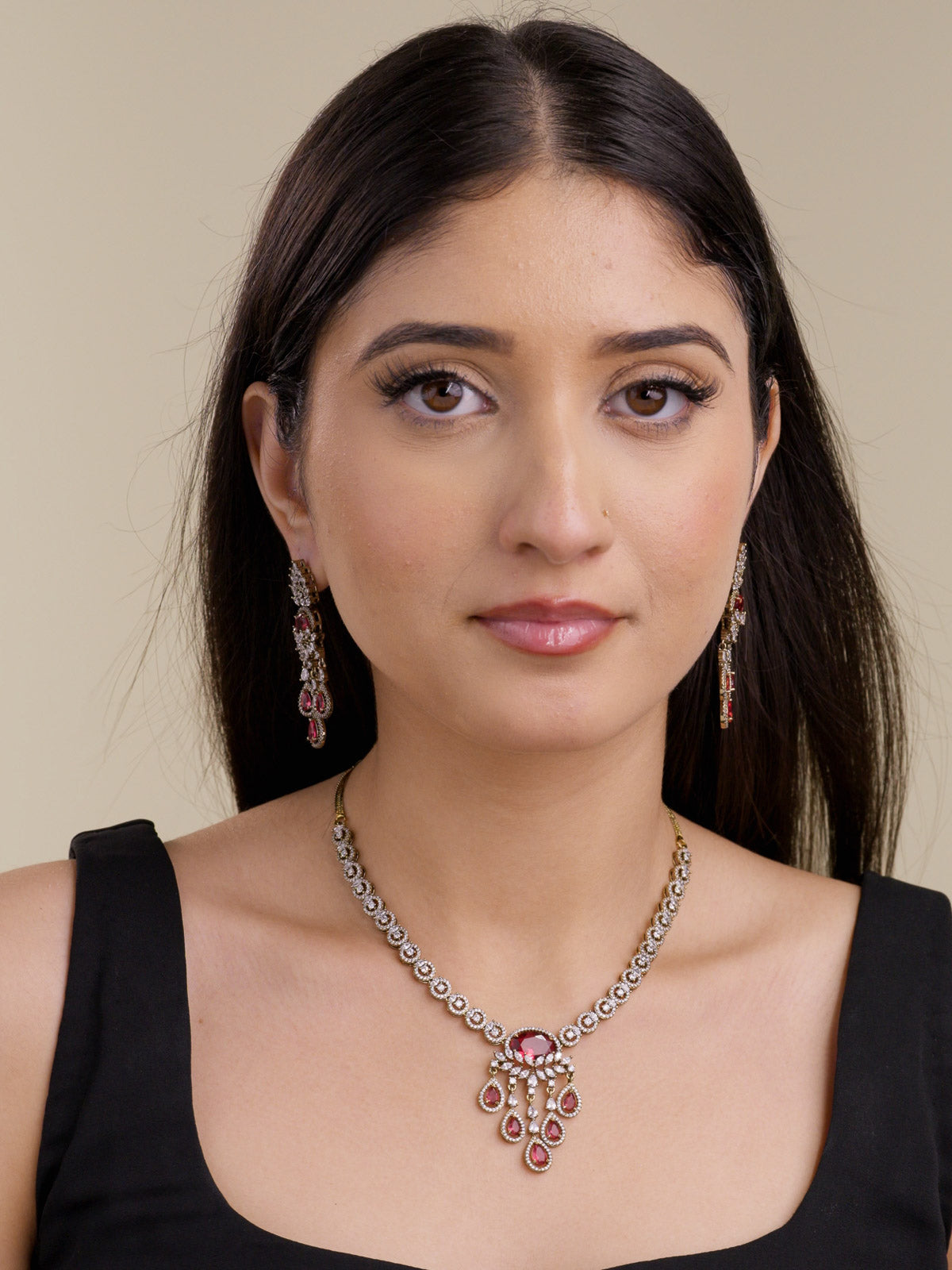 Model wearing an antique gold tone American Diamond necklace set with round CZ stone links, ruby red centre accents, matching drop earrings, and a black outfit in a front portrait shot.