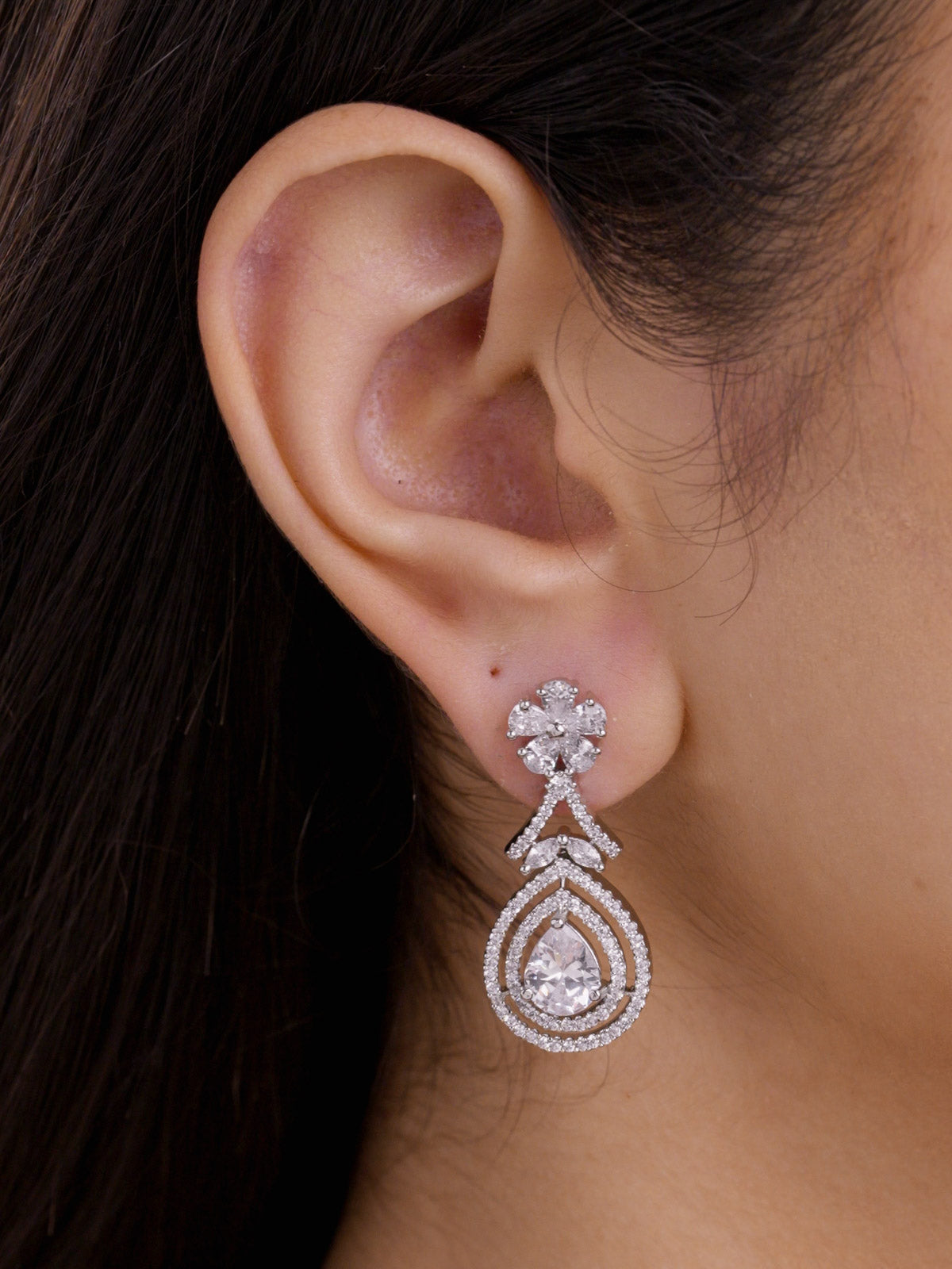 Close-up side view of a model wearing a silver tone American Diamond earring with a floral CZ stud, V-shaped connector, nested teardrop frame, and matching pear-shaped CZ centre stone.
