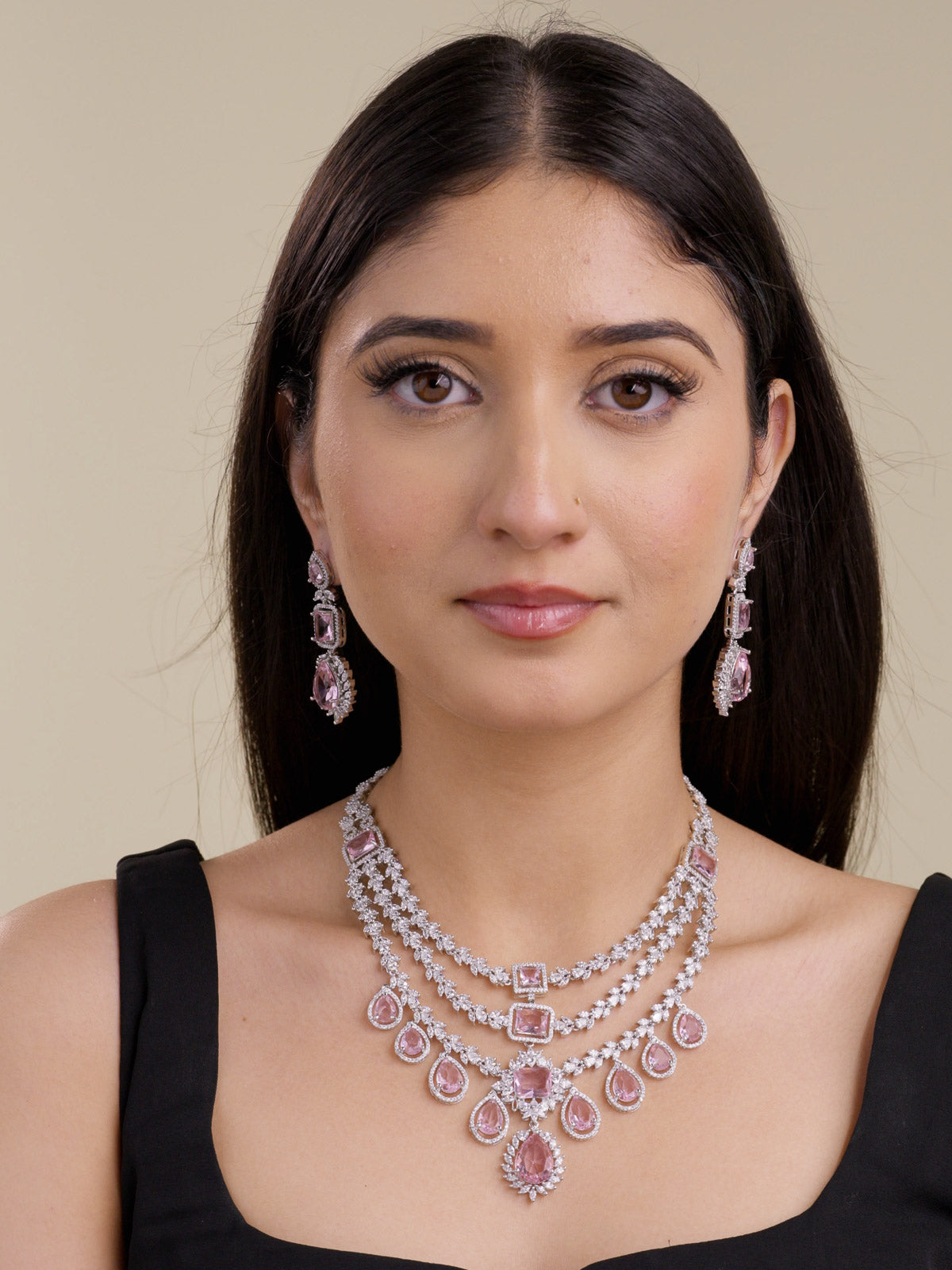 Front portrait of a model wearing a silver tone American Diamond necklace set with matching earrings, layered CZ stone detailing, pink rectangular and teardrop stones, and a centre drop pendant.