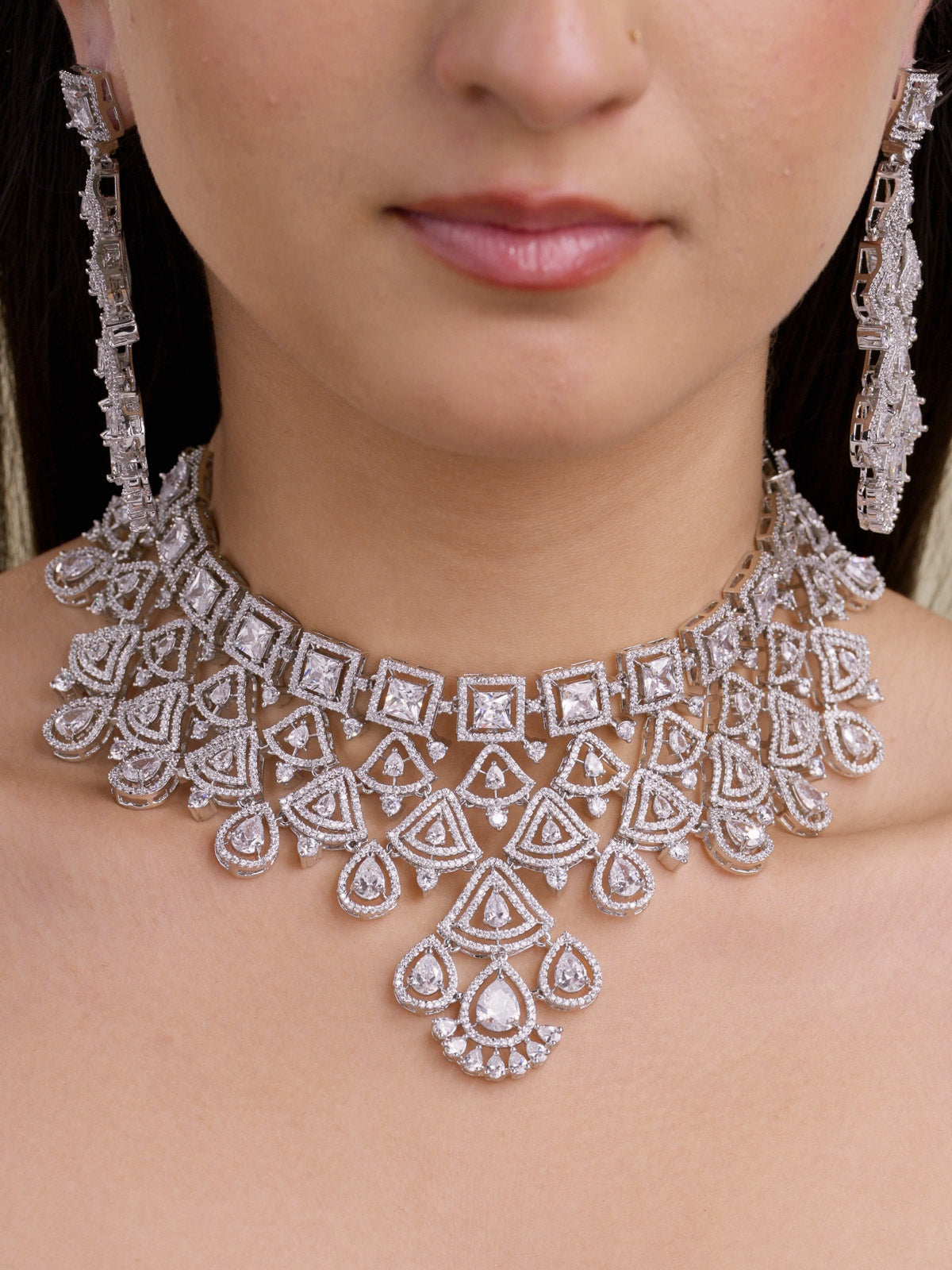 Close-up of a model wearing a silver tone American Diamond choker-style necklace set with square CZ stones, layered triangular detailing, pear-shaped lower drops, and matching long earrings.