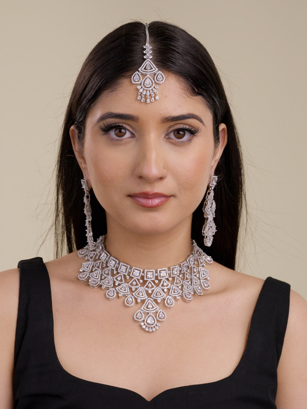 Front view of a model wearing a silver tone American Diamond choker-style necklace set with square CZ stones, layered triangular detailing, pear-shaped drops, matching long earrings, and a matching maang tikka.