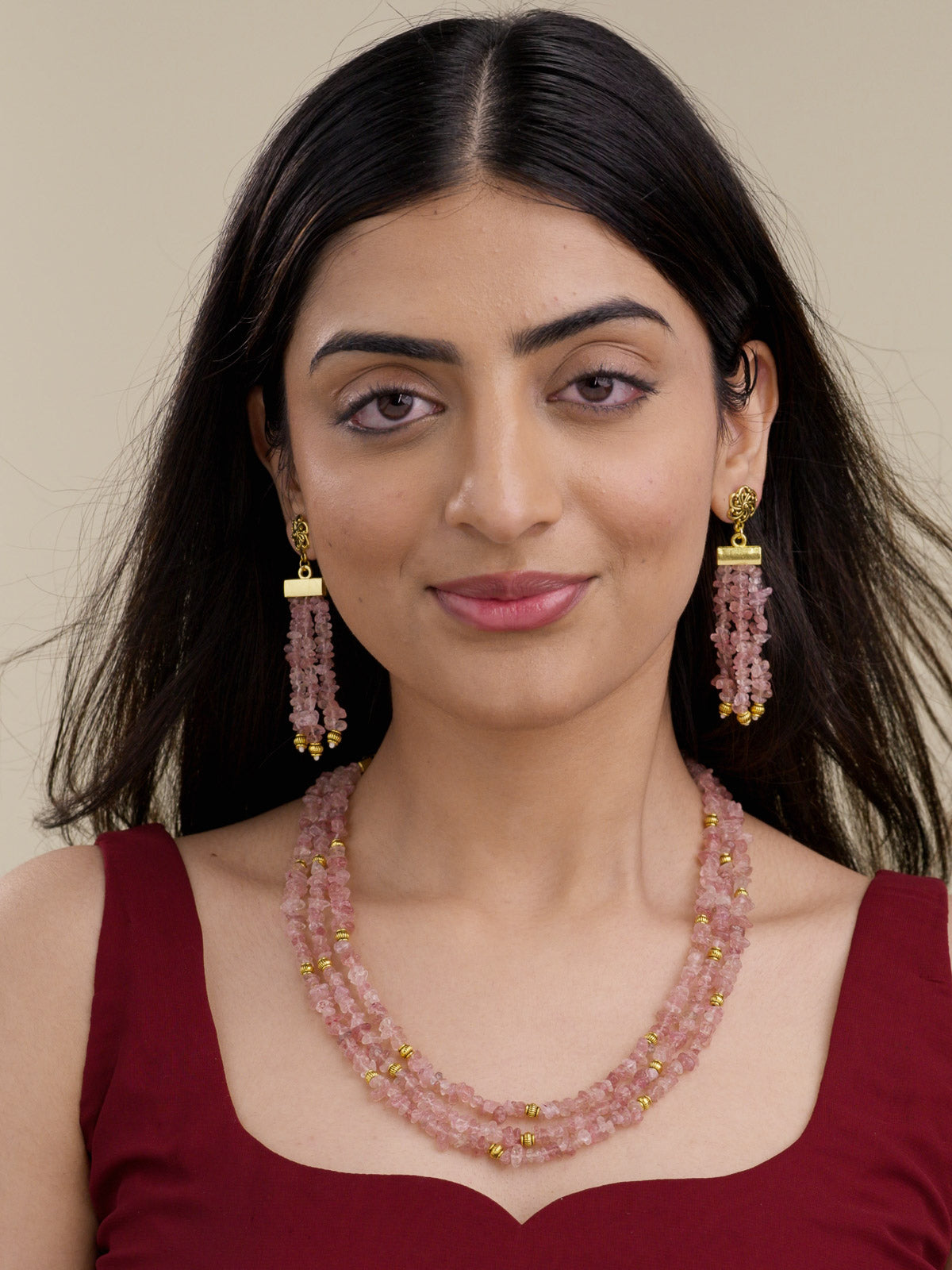 Model wearing a beadwork necklace set with layered chip-style pink bead strands, gold tone accents, and matching beaded tassel earrings