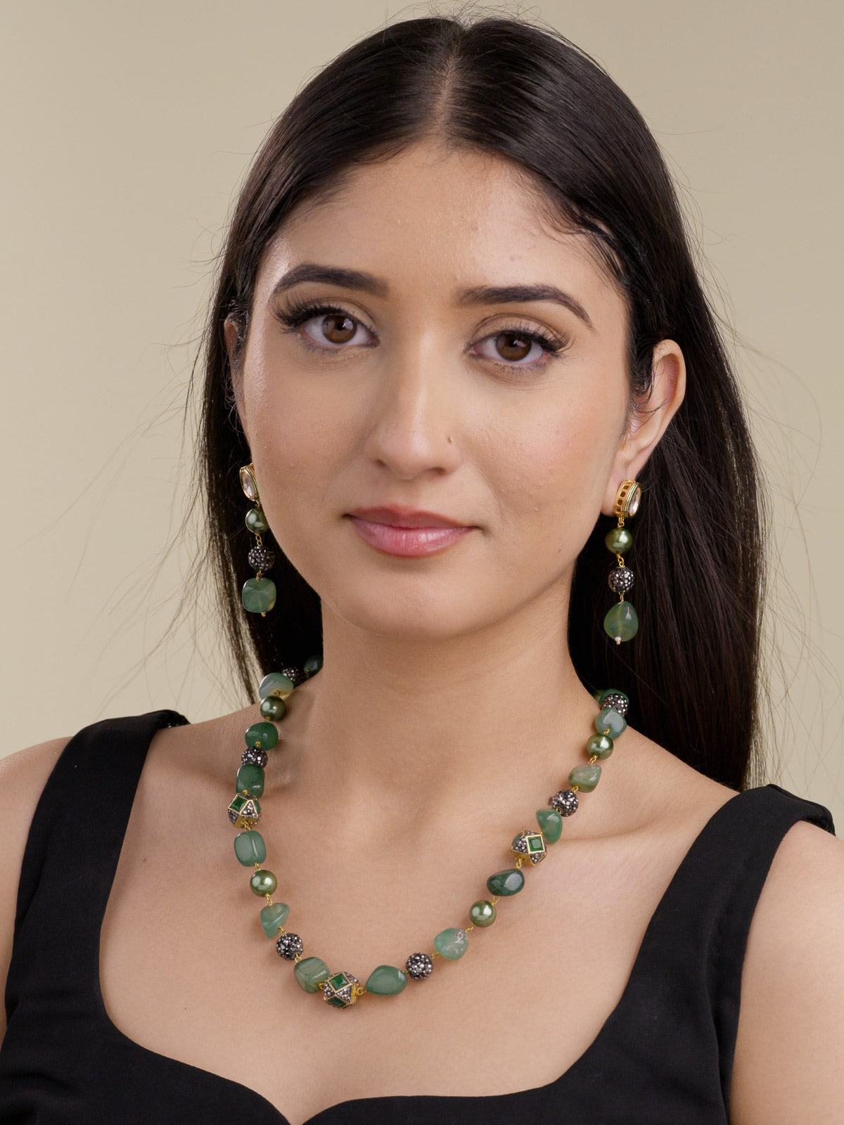 Model wearing gold tone beadwork necklace set with mixed green beads, green pearl-style accents, black crystal bead clusters, gold tone square accents, and matching drop earrings with kundan-look studs.