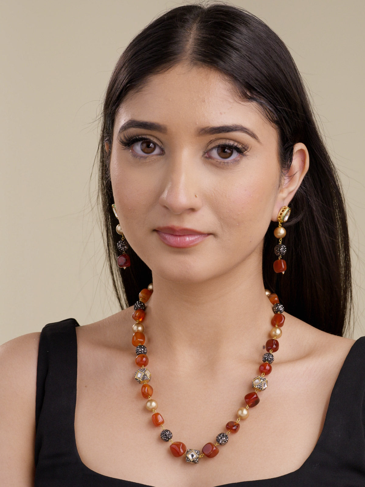 Model wearing gold tone beadwork necklace set with rust orange beads, pearl-style accents, black crystal bead clusters, gold tone square accents, and matching drop earrings with kundan-look studs.