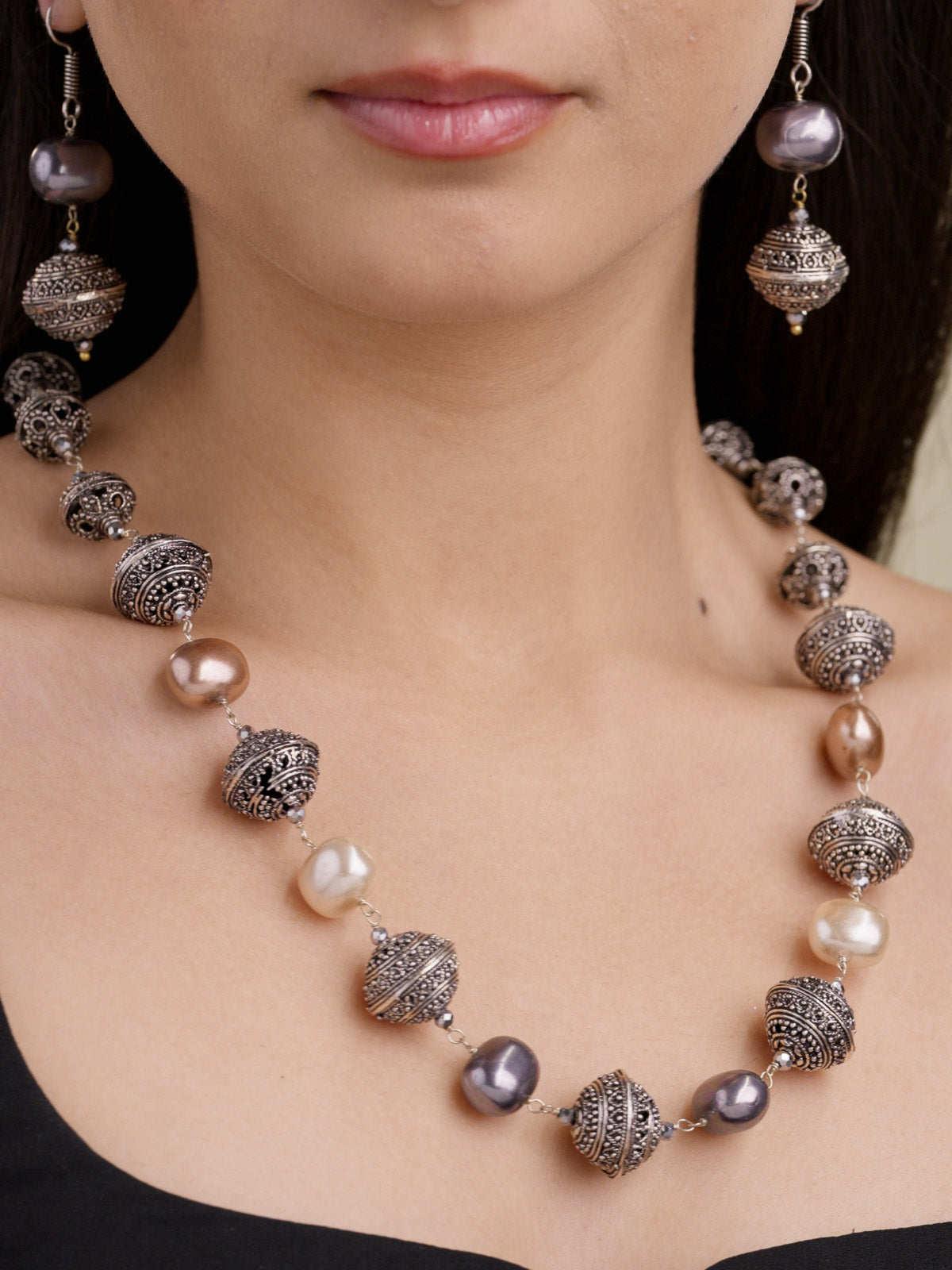 Beadwork necklace set in silver tone with textured metal beads, mixed grey, cream, and champagne pearl-style beads, and matching drop earrings on model close-up