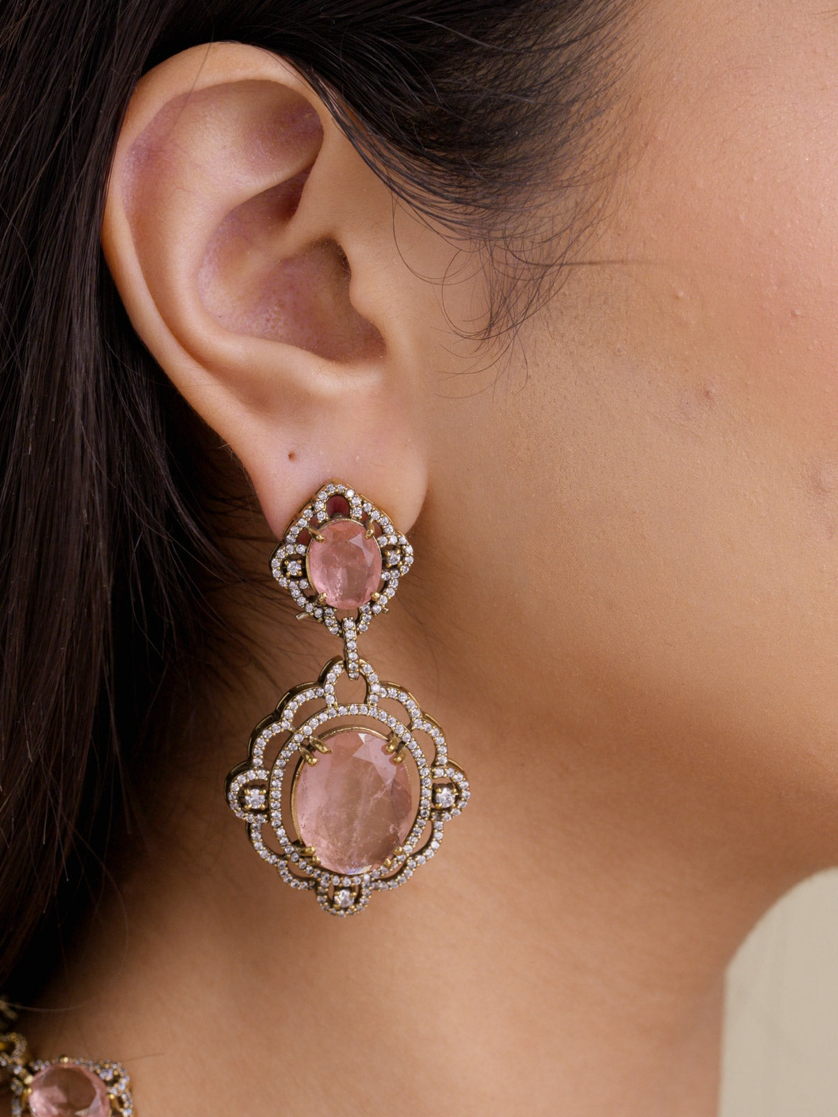 Close-up of a matching Fusion drop earring with peach-neutral stones, American Diamond-style detailing, and an antique gold tone setting worn on the ear.