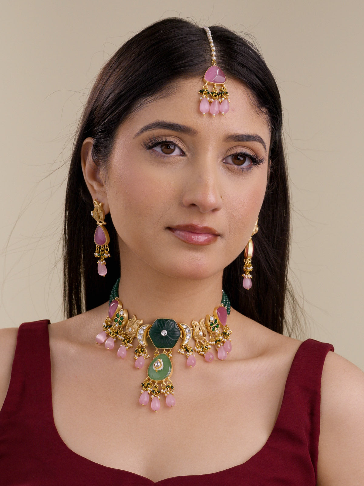 Model wearing Green Pink Fusion necklace set in gold tone with dark green carved centre, sage green lower pendant, pink teardrop drops, green bead strands, matching earrings, and maang tikka.