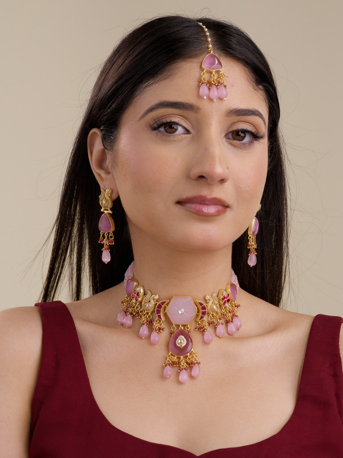 Model wearing Pink Ruby Fusion necklace set in gold tone with pale pink carved centre, deeper pink lower pendant, ruby accent stones, pink teardrop drops, matching earrings, and maang tikka.