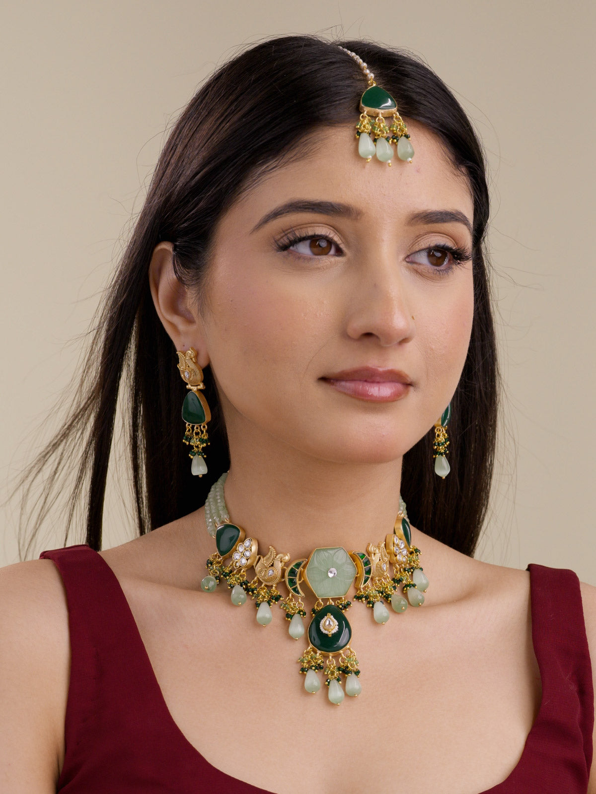 Model wearing Sage Green Fusion necklace set in gold tone with sage green carved centre, dark green lower pendant, pale sage teardrop drops, sage bead strands, matching earrings, and maang tikka.