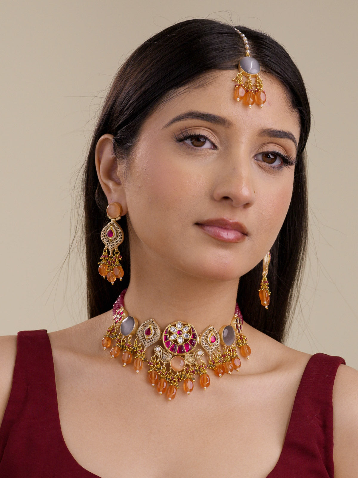 Front model view wearing Fusion necklace set in matte gold tone with ruby moon panels, kundan-look floral centre, grey round stones, lattice teardrop motifs, orange bead drops, matching earrings, and maang tikka.