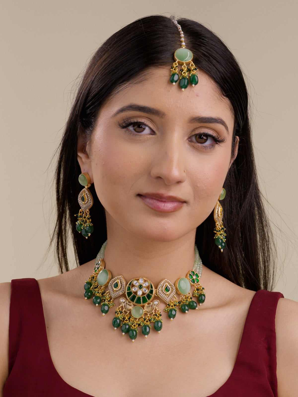 Front model view wearing Fusion necklace set in matte gold tone with green moon panels, white-stone floral centrepiece, sage green round stones, lattice teardrop motifs, dark green bead drops, matching earrings, and maang tikka.