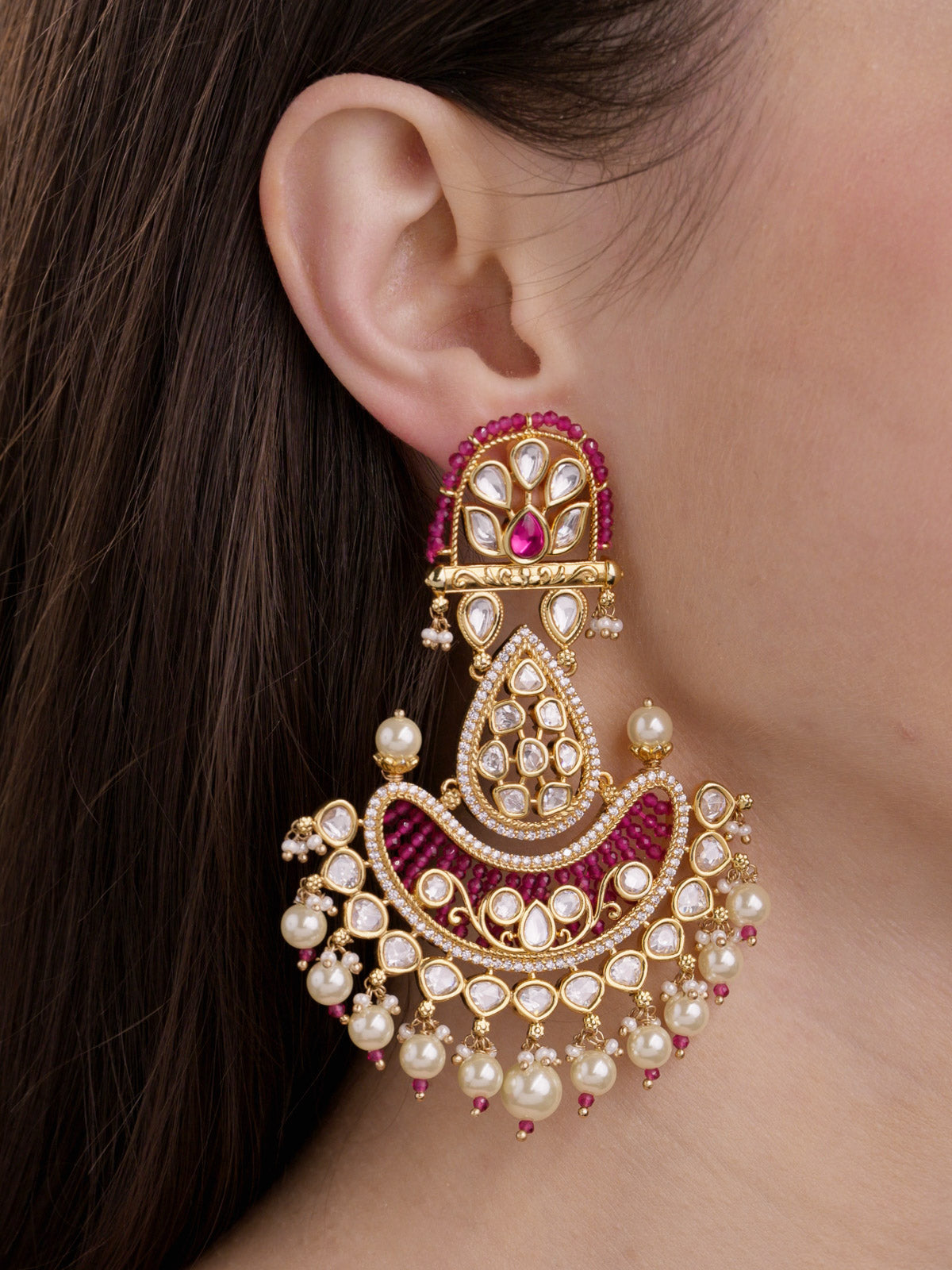 Close-up of a model wearing a statement Kundan earring in Gold Tone with ruby red accents, kundan-look teardrop stones, CZ detailing, and pearl drops.
