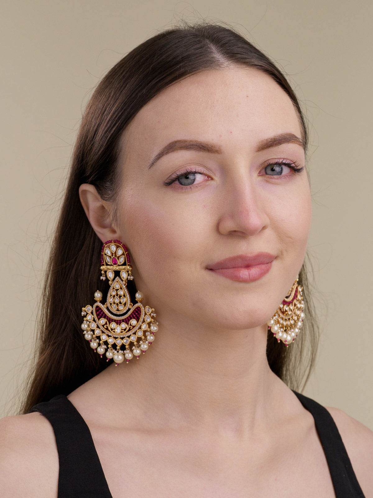 Model wearing statement Kundan earrings in Gold Tone with ruby red accents, kundan-look stones, American Diamond detailing, and pearl drops.