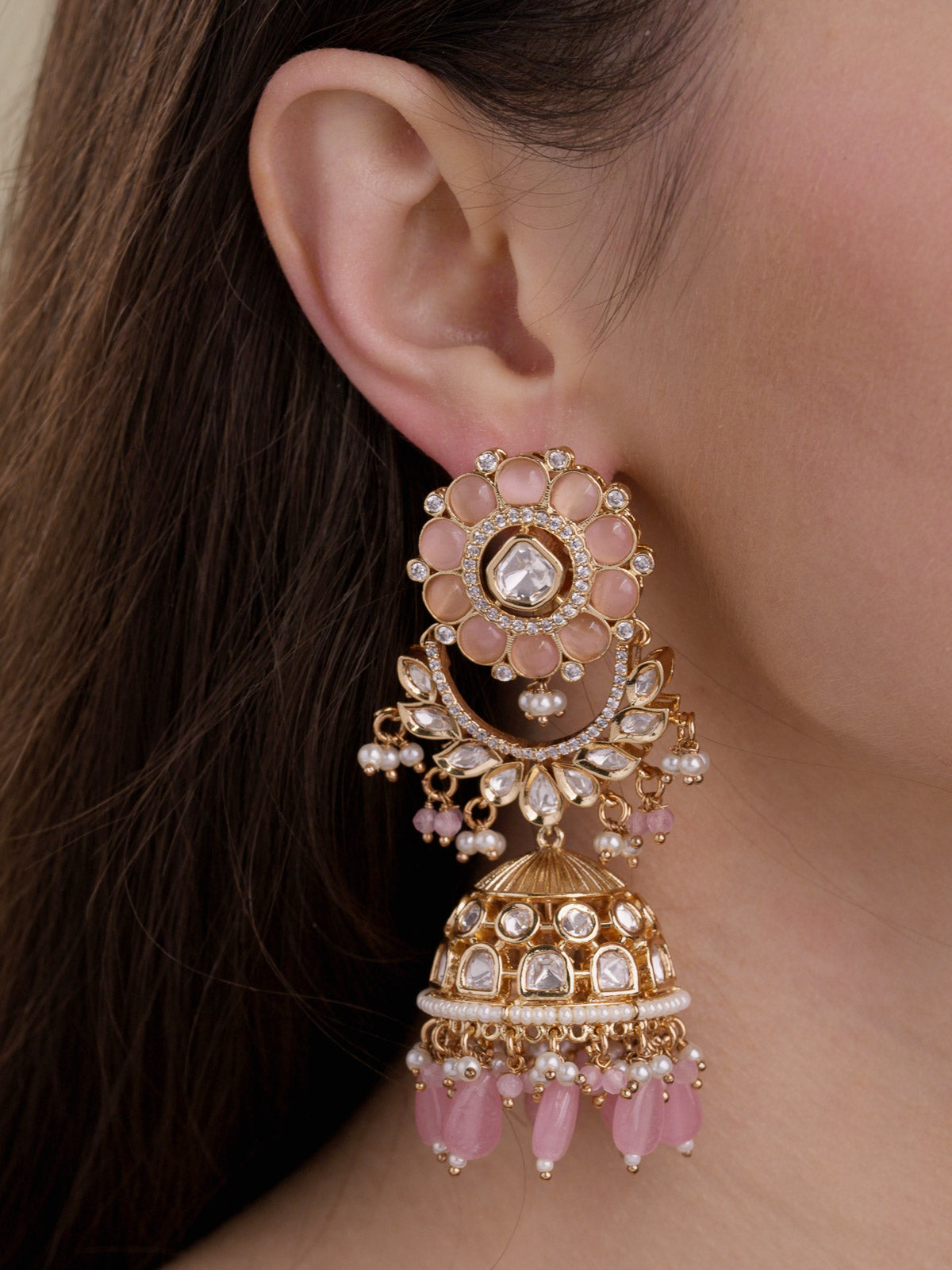 Close-up of a model wearing champagne gold tone Kundan jhumka earrings with a pink floral stud, AD detailing, pearl-style accents and pink bead drops.