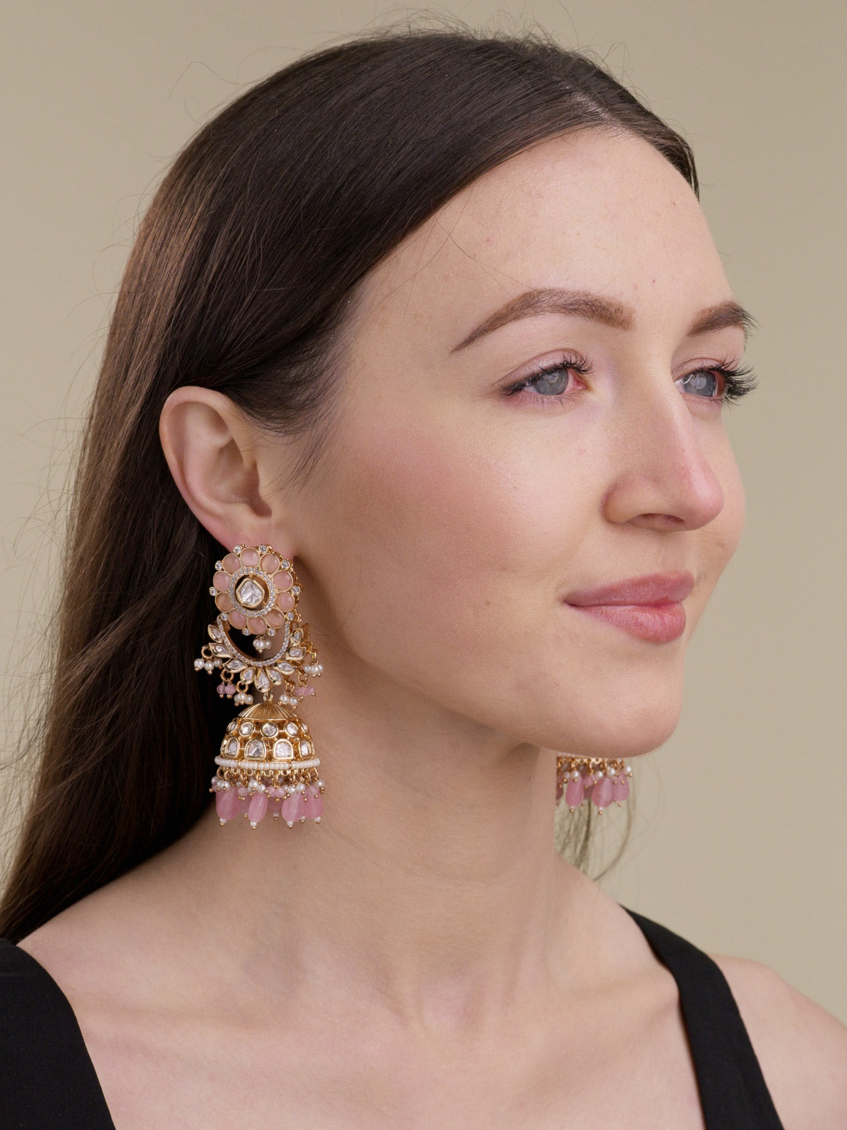 Model wearing champagne gold tone Kundan jhumka earrings with AD detailing, pink floral stud, pearl-style accents and pink bead drops.