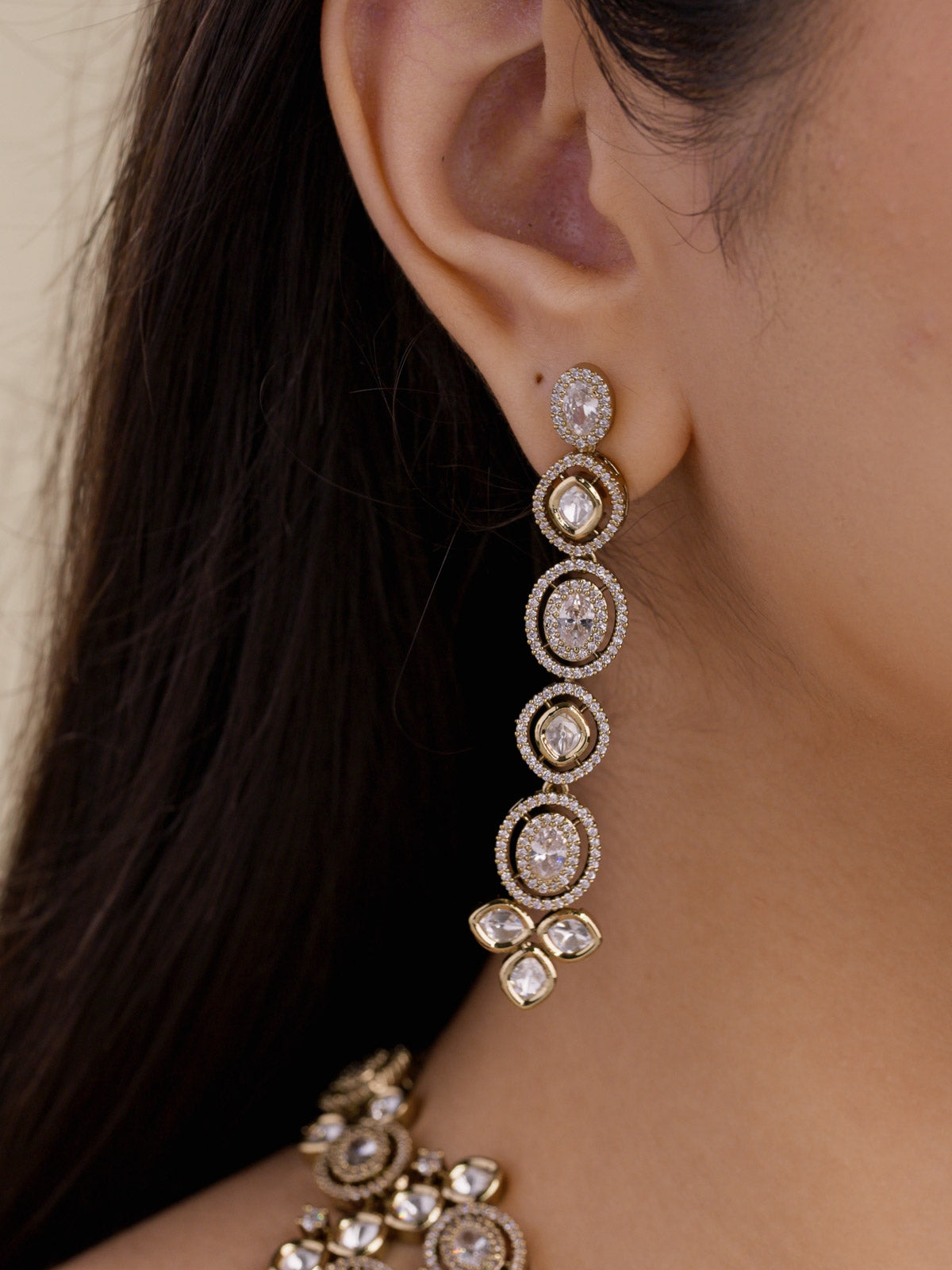 Kundan necklace set earrings with round kundan-look stones and American Diamond detailing in antique gold tone, long drop design, close-up worn on model ear