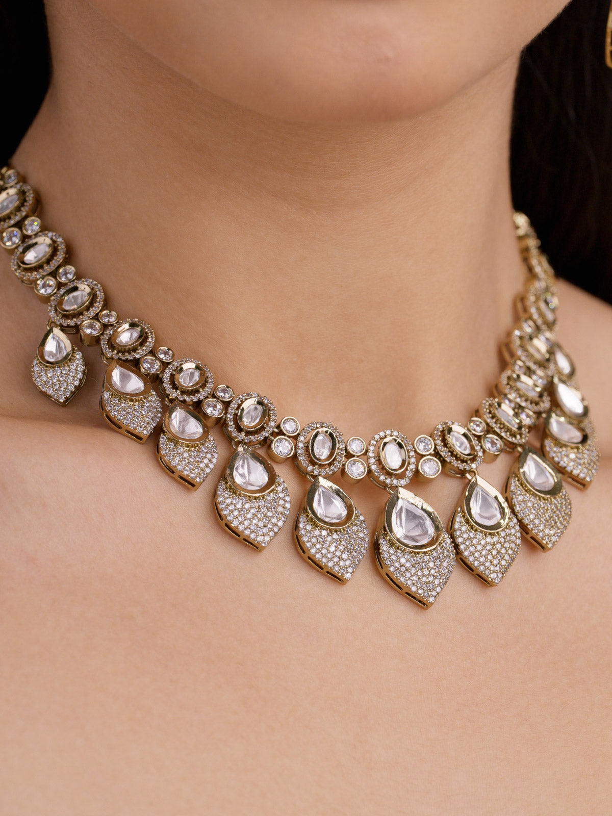 Kundan necklace set with oval kundan-look stones and petal-shaped drop design, with American Diamond detailing in antique gold tone, worn on model neckline