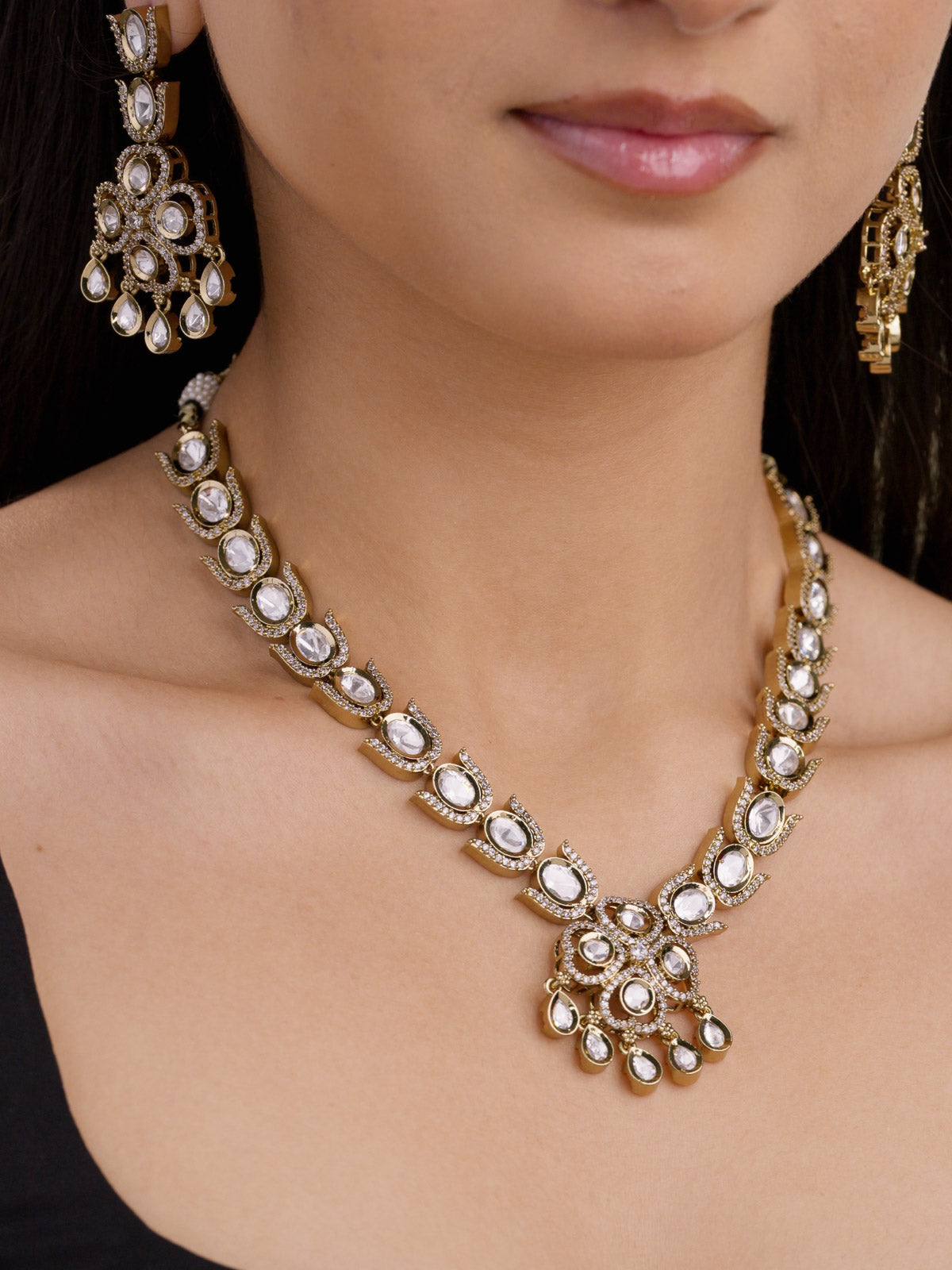 Close-up of kundan necklace with repeating oval units and center cluster drop with american diamond detailing in antique gold tone on model
