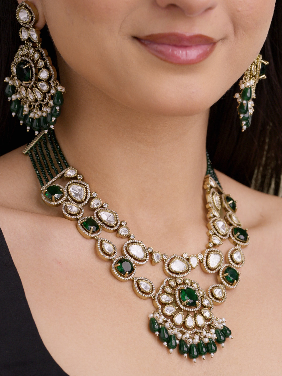 Close-up of antique gold tone Kundan necklace set with green stones, American Diamond outline detailing, matching earrings, pearl-style accents, and green bead drops on model