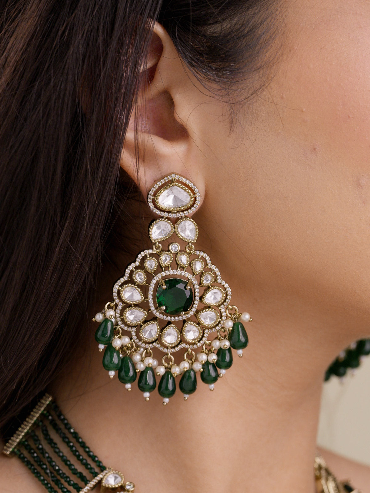 Close-up of antique gold tone Kundan earring with green centre stone, American Diamond outline detailing, pearl-style accents, and green bead drops on model