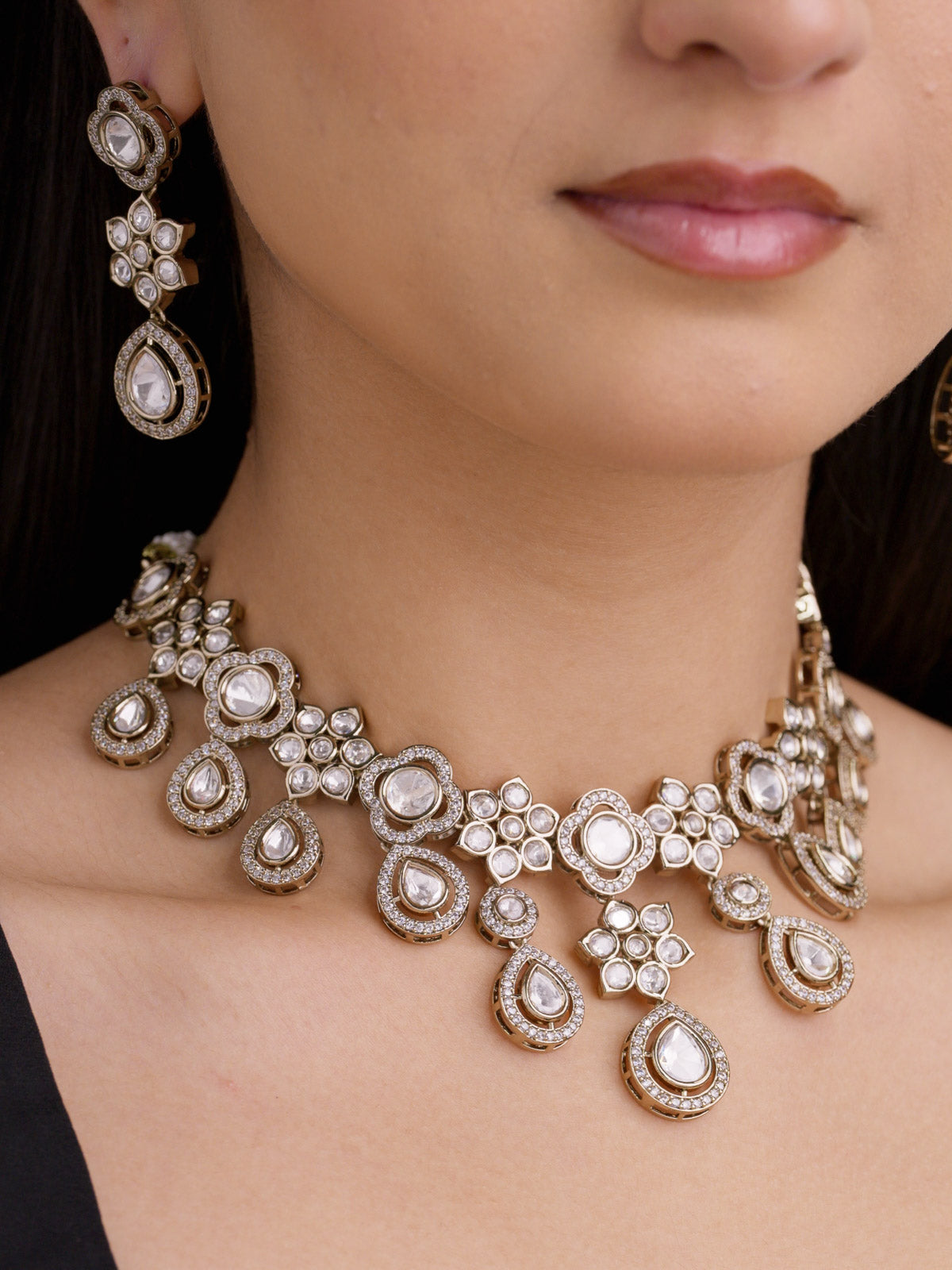Close-up of Kundan necklace set on model with layered teardrop drops, floral-style stone clusters, American Diamond detailing, antique gold tone, and neutral stones, and matching earrings