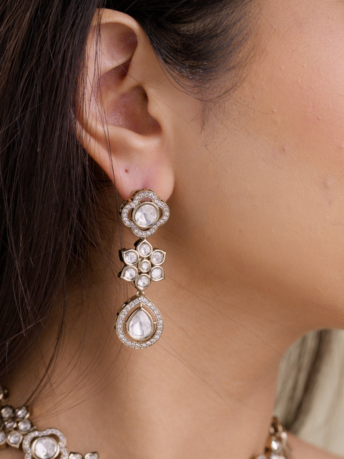 Close-up of Kundan earring with teardrop drop, floral stone centre, American Diamond border detailing, antique gold tone, and neutral stones