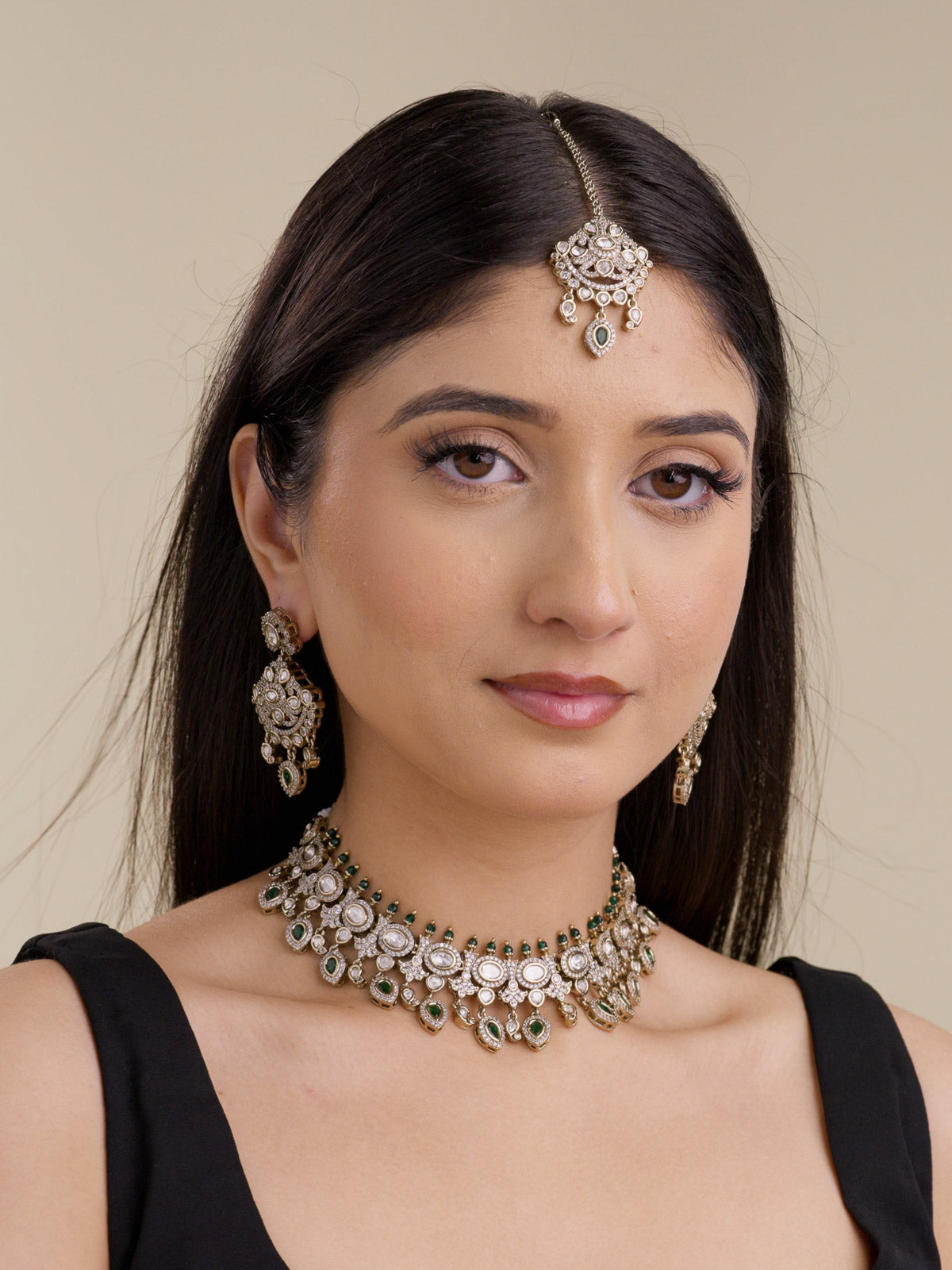 Front model view wearing a collar-style antique gold tone Kundan necklace set with green stones, matching earrings, and maang tikka.