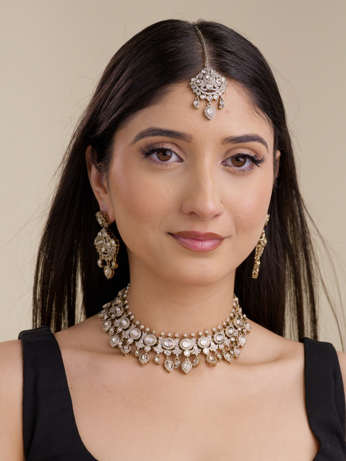 Front model view wearing a collar-style antique gold tone Kundan necklace set with neutral kundan-look stones, matching earrings, and maang tikka.