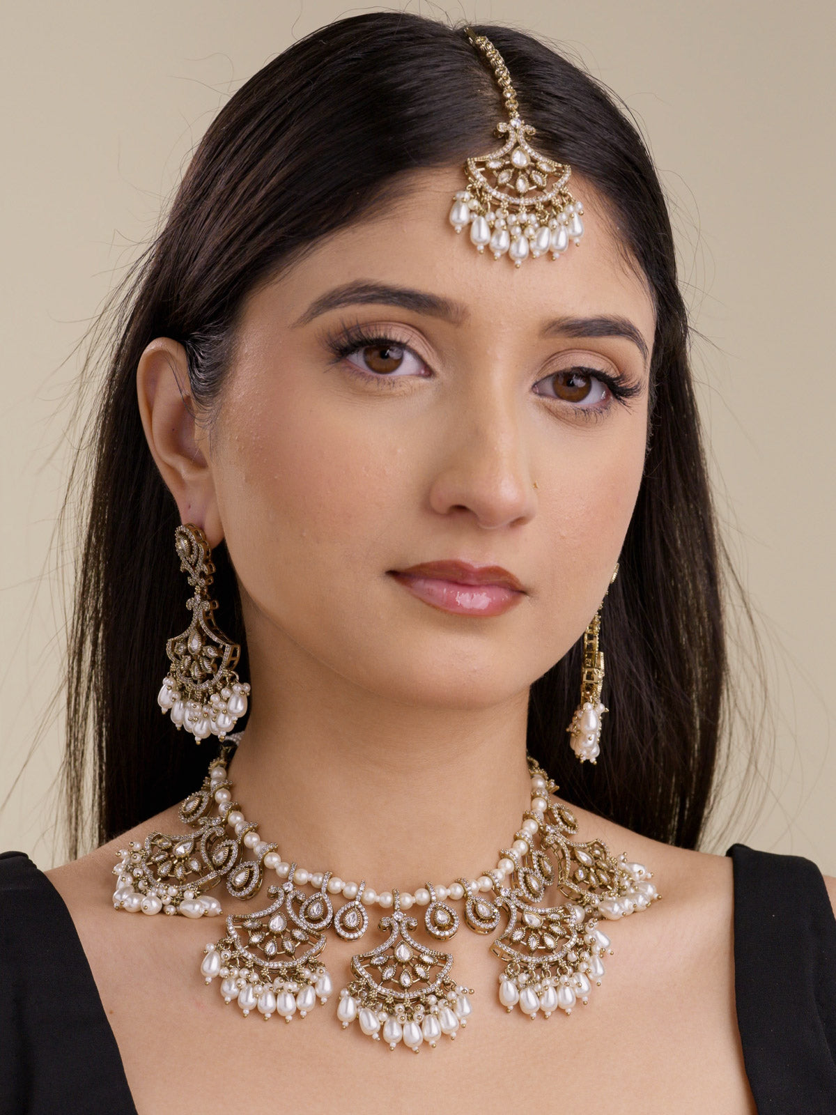 Model wearing a neutral Kundan necklace set in antique gold tone with matching earrings and tikka, featuring pearl-style drops, kundan-look stones, and American Diamond detailing.