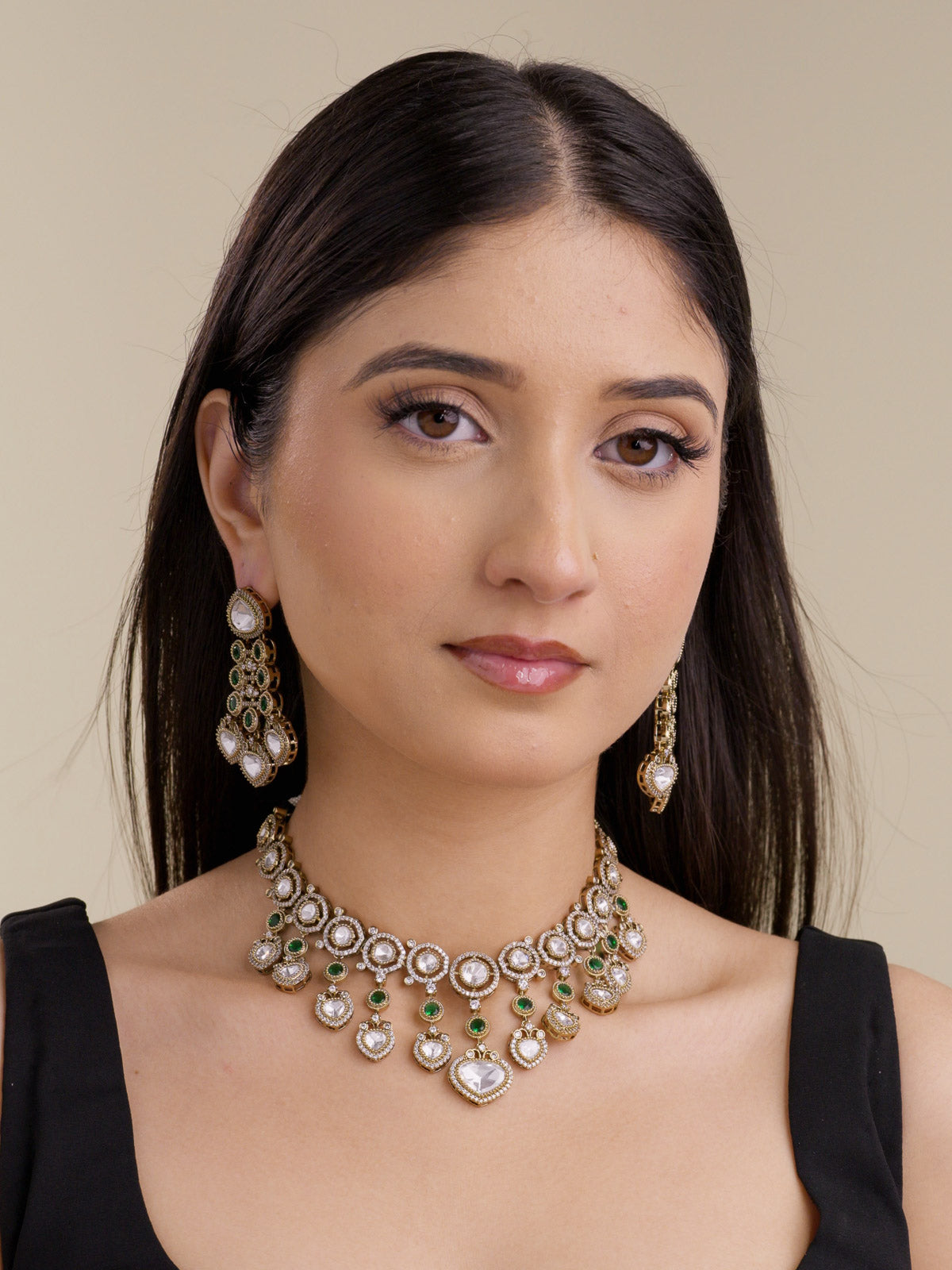 Model wearing an antique gold tone Kundan necklace set with green accents, kundan-look stones, American Diamond detailing, and matching earrings.