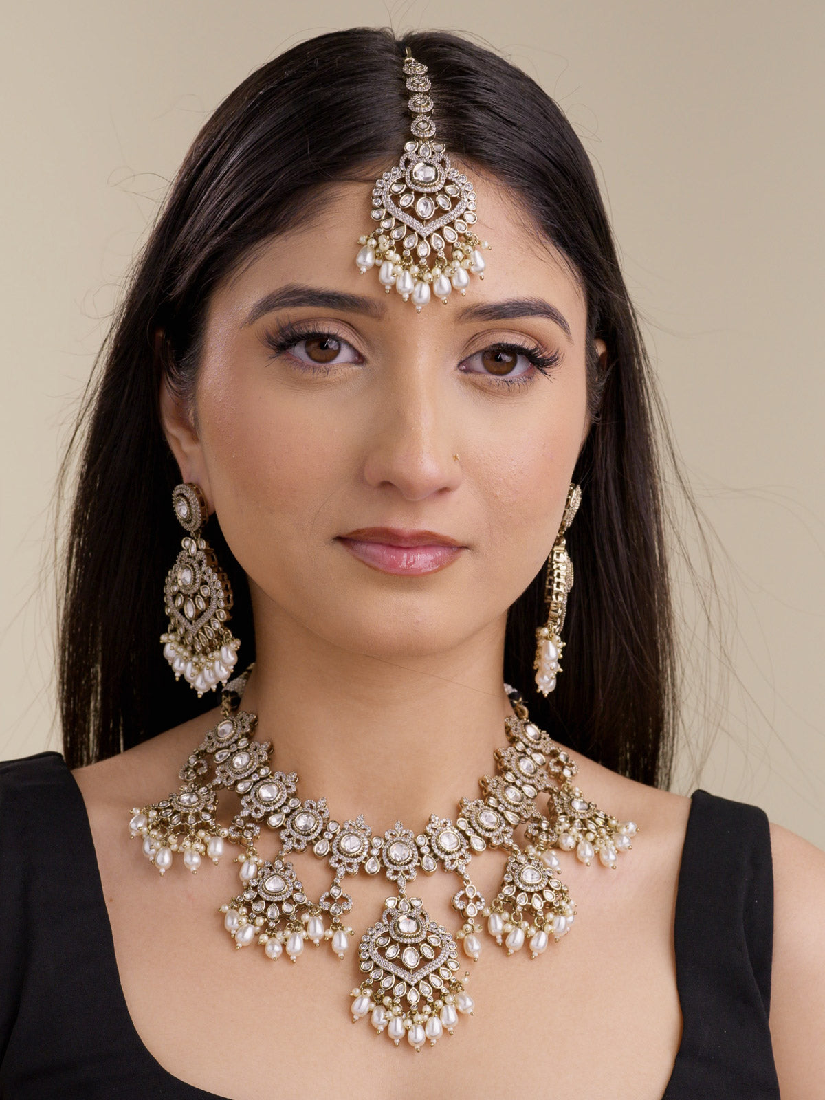 Model wearing a neutral Kundan necklace set with matching earrings and maang tikka, antique gold tone detailing, white stonework, pearl-style accents, and ivory bead drops