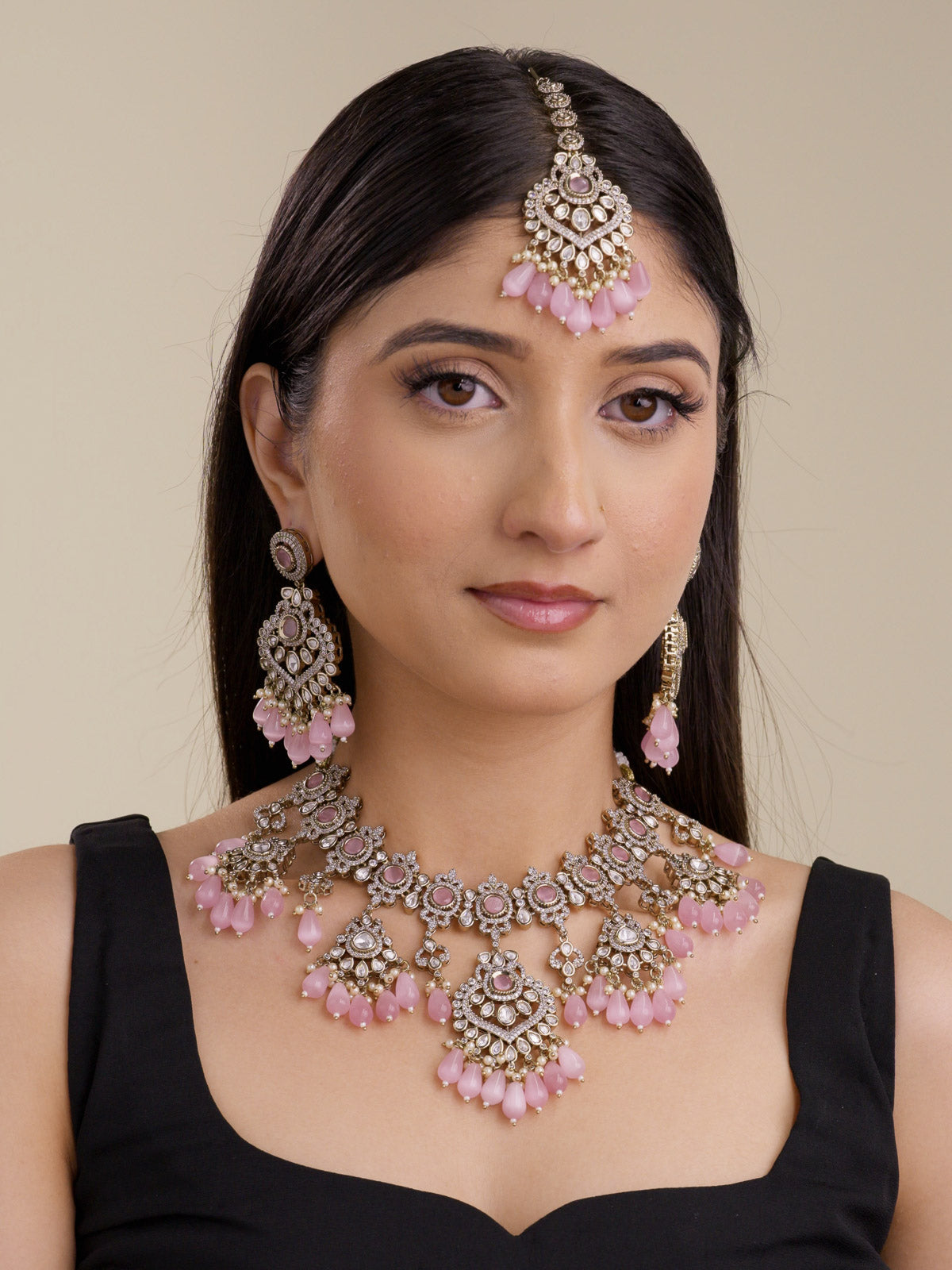 Model wearing a pink Kundan necklace set with matching earrings and maang tikka, antique gold tone detailing, white stonework, pearl-style accents, and pink bead drops
