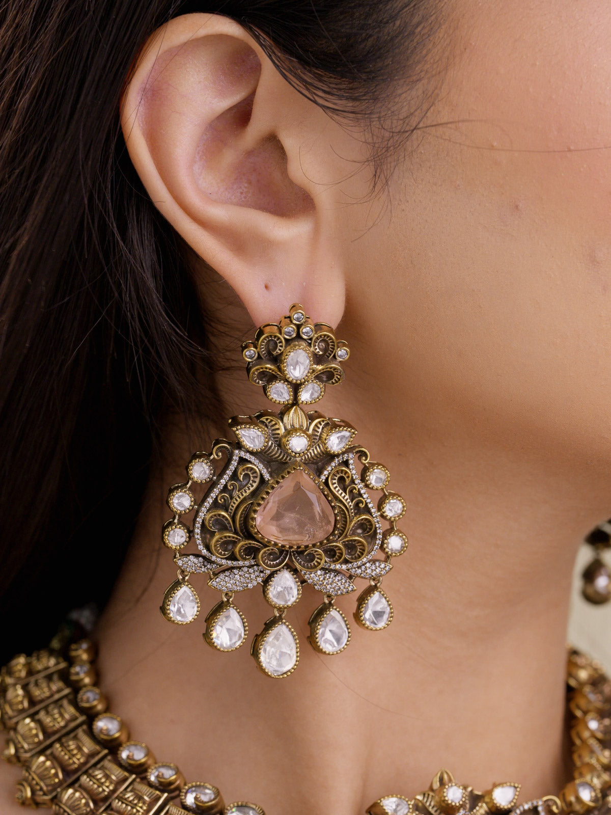 Close-up of matching Kundan earrings in antique gold tone with a blush teardrop centre, lotus-inspired fan motif, kundan-look drops, and American Diamond detailing.