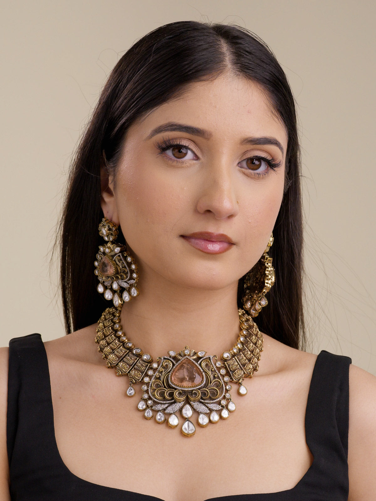Model wearing a bold Kundan necklace set in antique gold tone with matching earrings, textured collar panels, lotus-inspired fan centre, blush teardrop stone, and kundan-look drops.