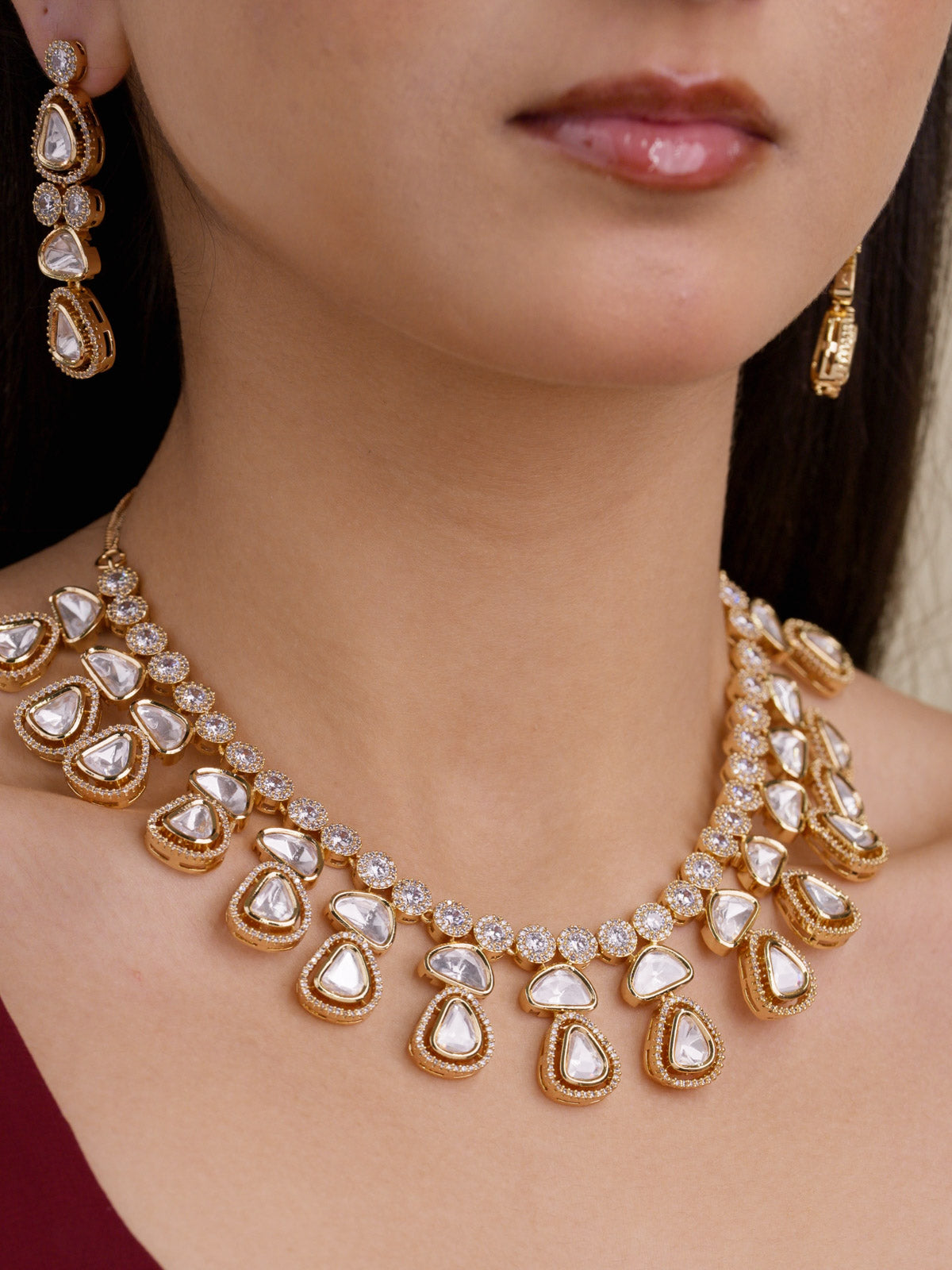 Close-up of model wearing a Kundan necklace set with a champagne gold tone finish, American Diamond top strand, neutral teardrop kundan-look stones, and matching drop earrings.
