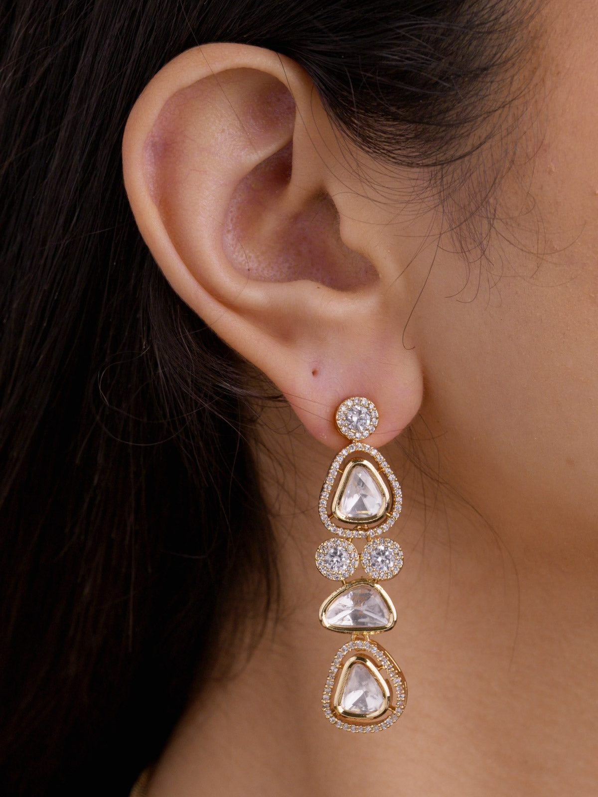 Close-up of model wearing a champagne gold tone drop earring with round American Diamond detailing and neutral teardrop kundan-look stones.